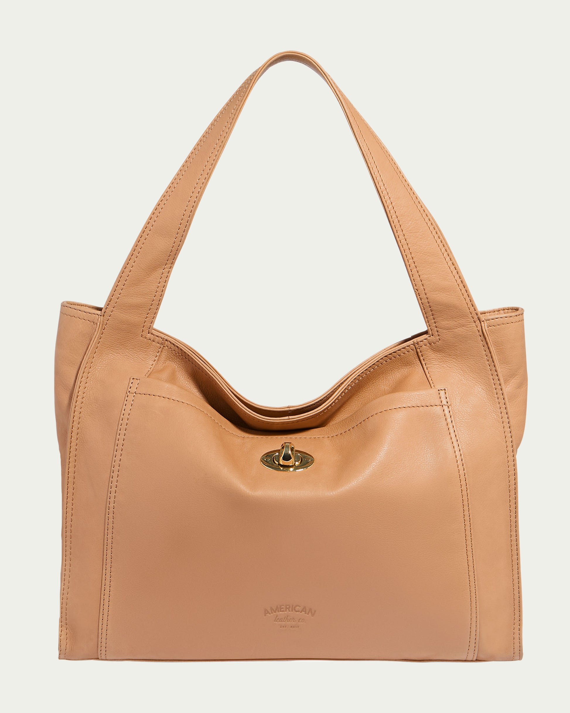 The Plymouth Ziptop Tote by American Leather Co. is a genuine leather bag in tan, featuring two handles and a front flap with a gold turn-lock closure. The brand name is embossed at the bottom, accompanied by a discreet zipper pocket. Set against a light cream background, it embodies elegance and functionality.