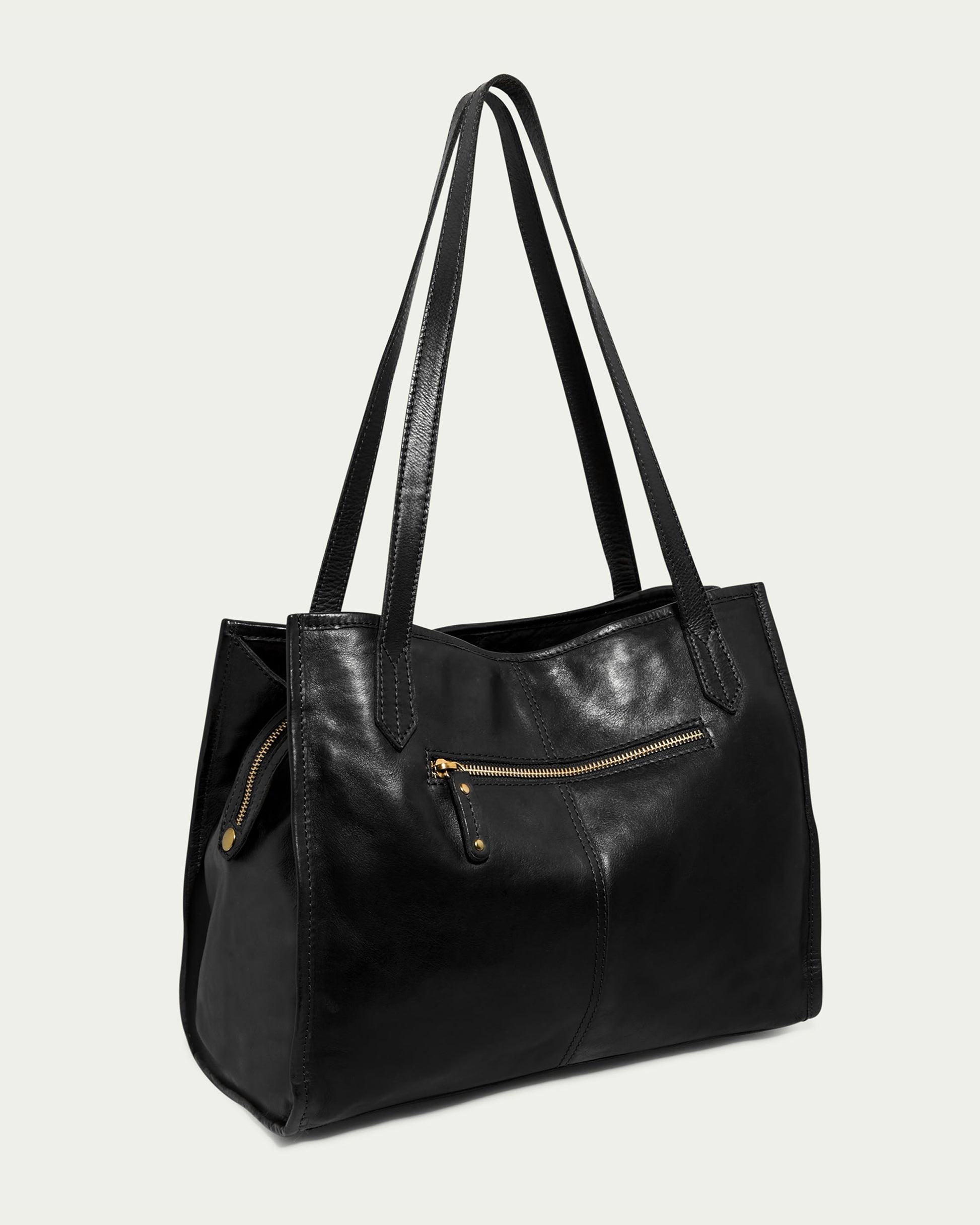 The Sandy Woven Triple Entry Satchel by American Leather Co. is a chic black tote bag showcased on a light background. It features long handles, a front zippered pocket adorned with a gold zipper, and meticulous stitching details. Made from genuine leather, it boasts a sleek, minimalist design with a soft and slightly glossy finish.