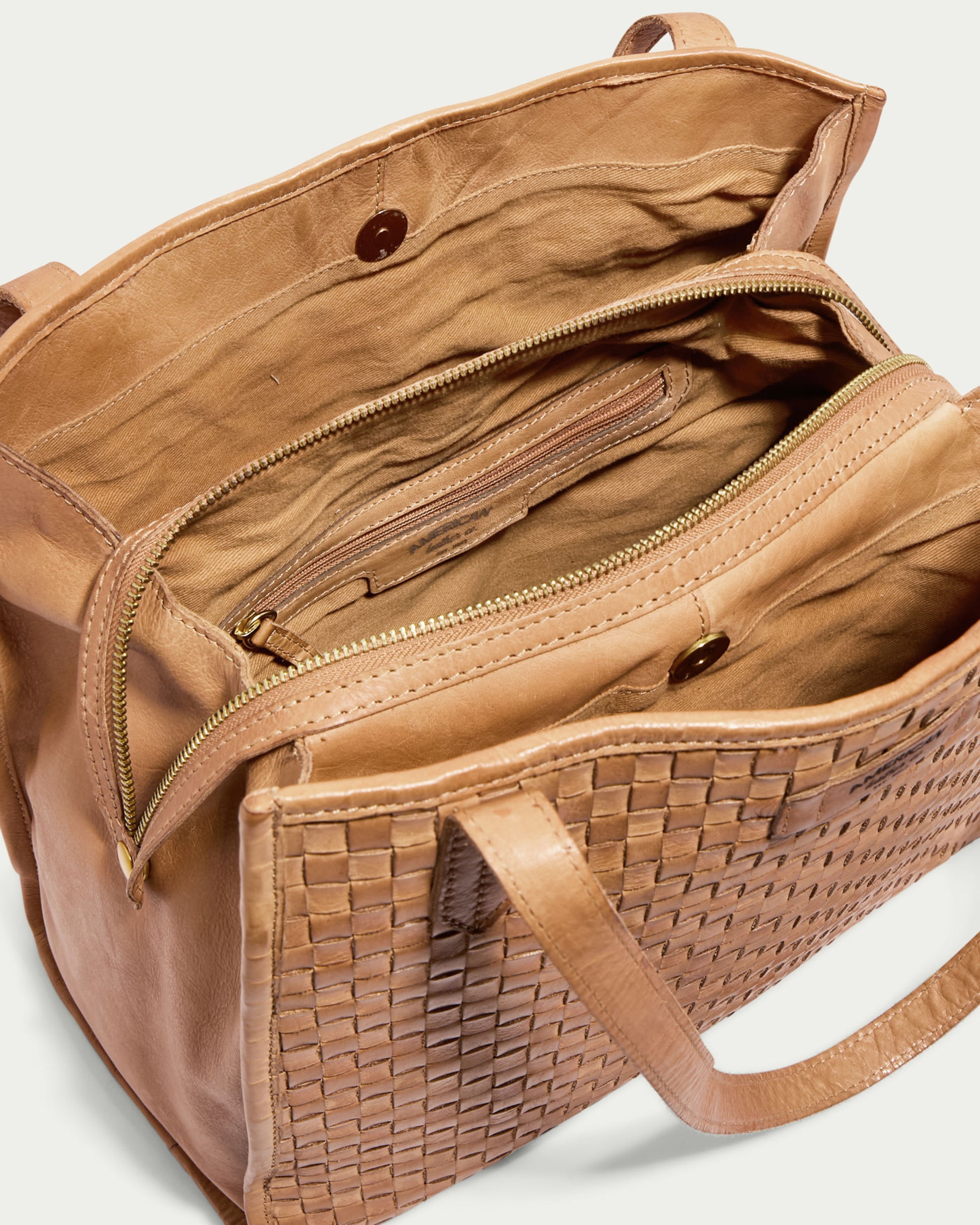 Introducing the Sandy Woven Triple Entry Satchel by American Leather Co., a tan leather bag with intricate woven detailing and multiple compartments. The interior features a main zippered section, a smaller zippered pocket, and an open pocket with button closure. Made from genuine leather, it has two handles and reveals a spacious heritage interior when opened.