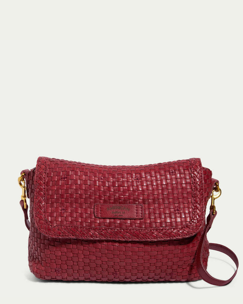 A limited edition handbag, the Summers Woven Crossbody by American Leather Co. features a flap closure and an adjustable strap. This red woven crossbody boasts gold-tone hardware accents and a small rectangular label on the front flap, with intricate interwoven detailing that provides a textured appearance.