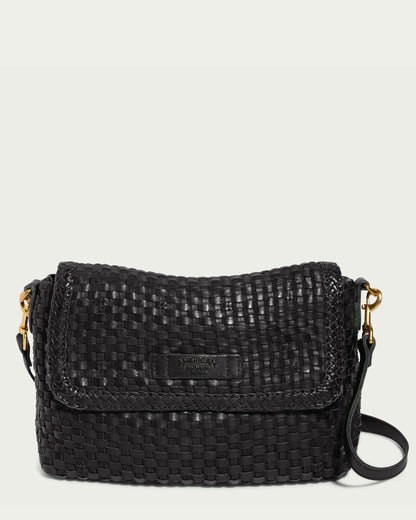 Introducing the Summers Woven Crossbody, a black woven leather crossbody bag with a flap closure. This limited edition piece features a shoulder strap with gold metal clasps attached on both sides, and proudly displays the brand name "American Leather Co." embossed on a small leather patch on the front.