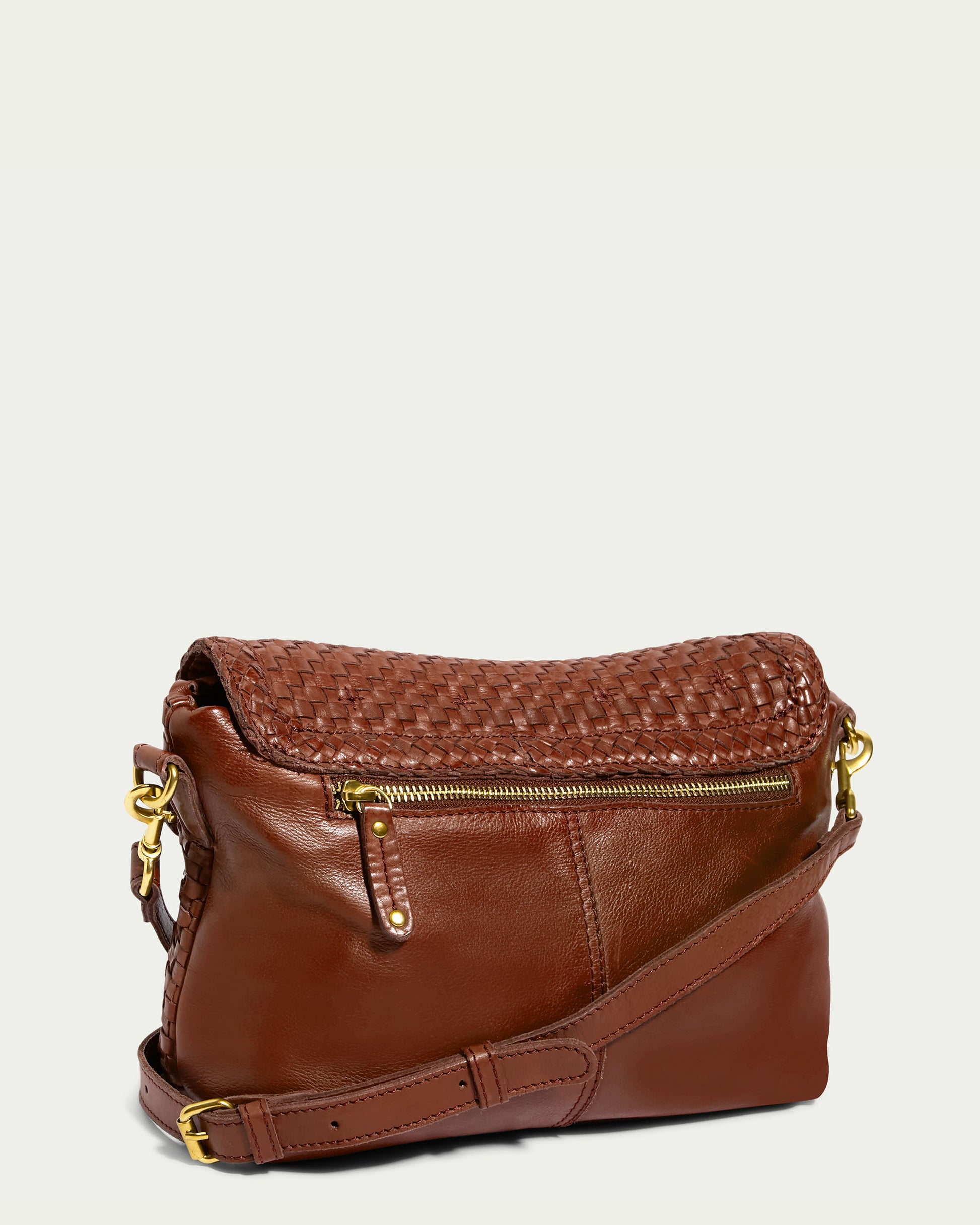 Introducing the Summers Woven Crossbody by American Leather Co. - a stylish, brown genuine leather bag with a distinctive woven flap closure. It boasts a gold zipper pocket at the back, an adjustable and detachable shoulder strap embellished with gold hardware, and intricate stitched detailing. This versatile crossbody bag is perfect for any occasion.