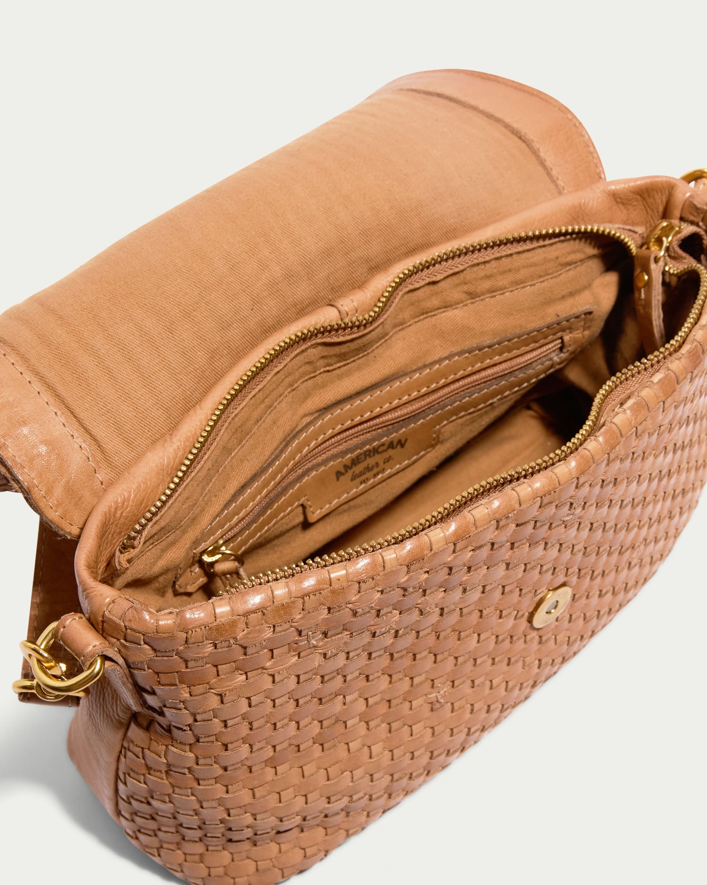 The Summers Woven Crossbody by American Leather Co. in open tan features visible internal compartments, including a zipper pocket, card slot, and main storage area. Made from genuine leather with a gold clasp and hardware, it's the perfect stylish yet functional woven flap crossbody.