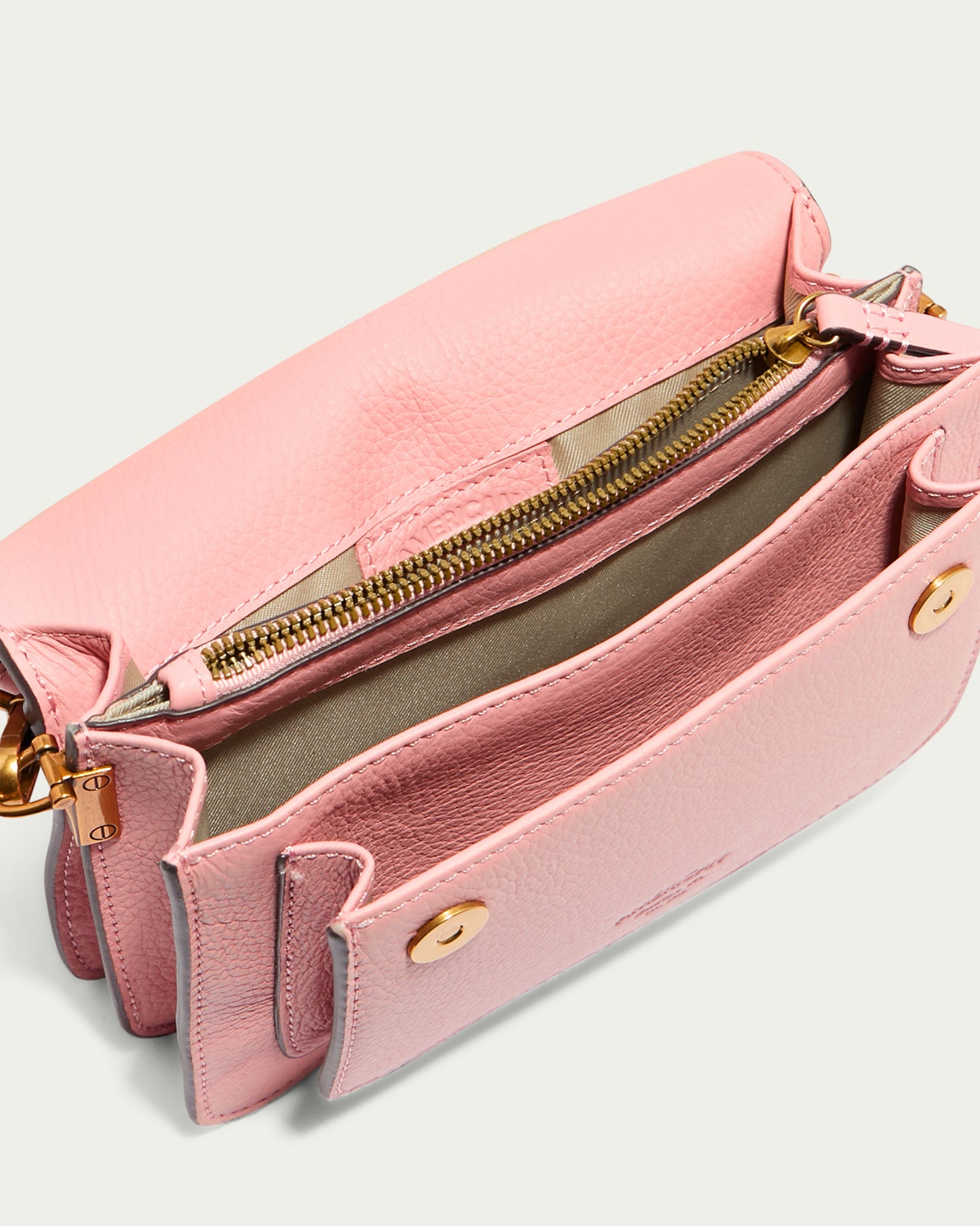 The Troy Acordian Crossbody by American Leather Co. is displayed as an open pink crossbody purse with a textured finish, crafted from genuine leather. It includes a gold zipper on the inner compartment and two snap buttons on the front pocket, with a beige interior lining.