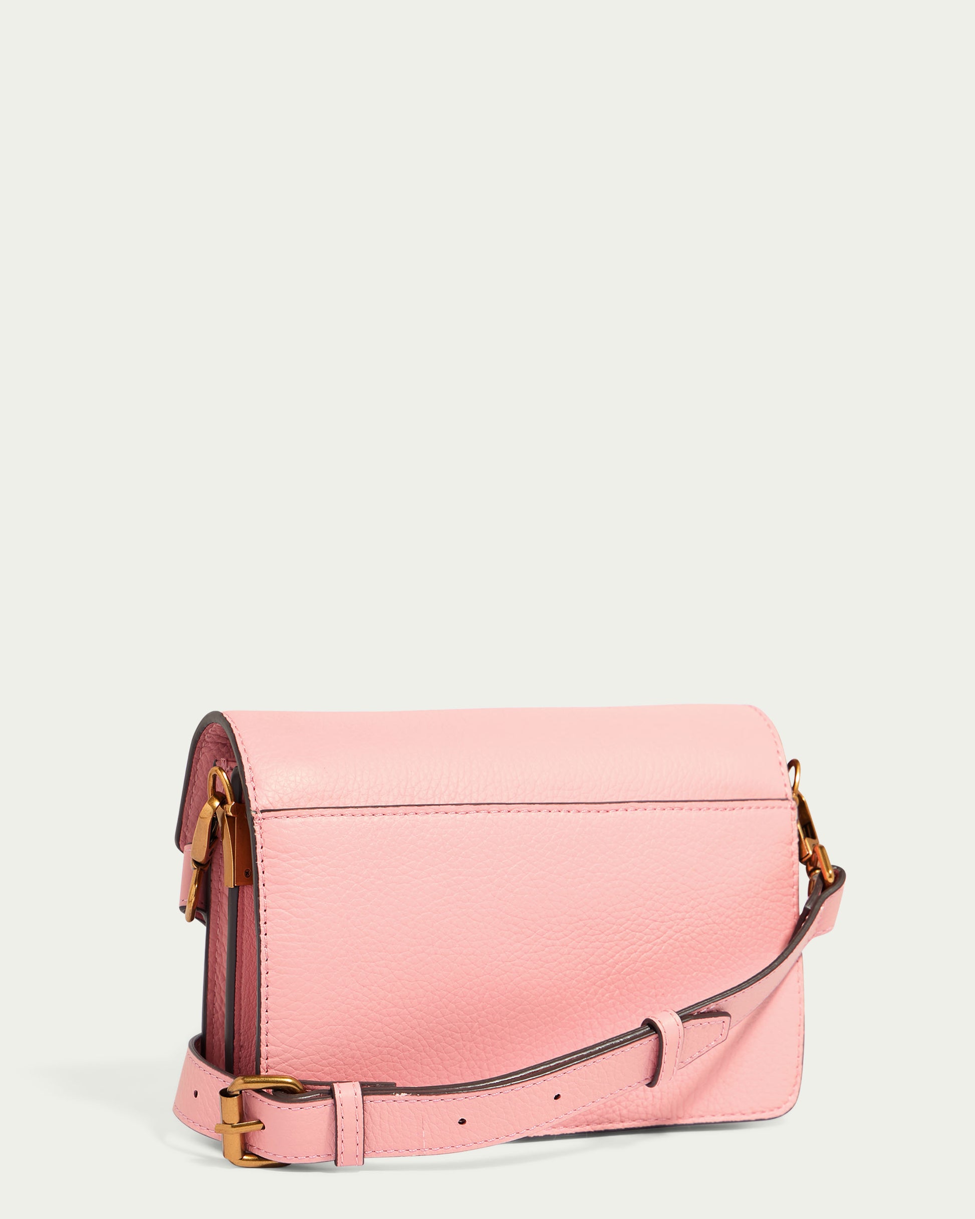 The Troy Acordian Crossbody by American Leather Co. is a pink handbag made from genuine leather, showcasing a flap closure and an adjustable strap on a light backdrop. The gold-tone hardware enhances its elegant design.