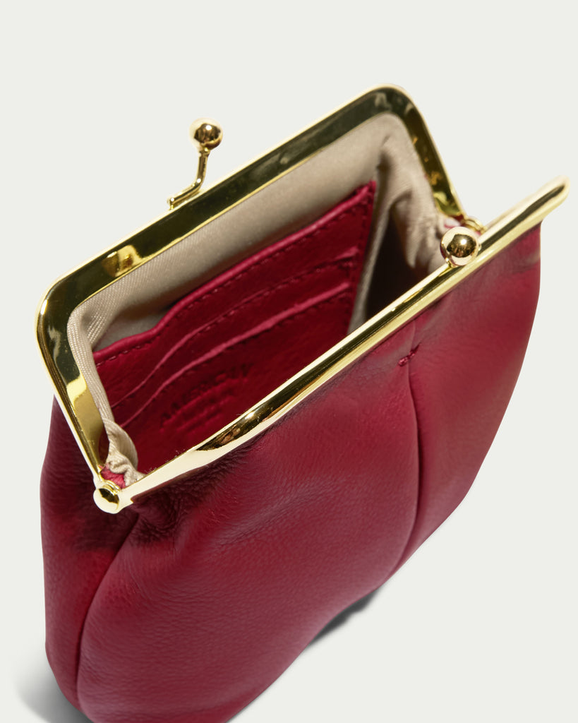 An item from the Cleveland Collection, the Wolfe Frame Kisslock With CC Slots by American Leather Co., is displayed. This compact and open red leather coin purse has a brass frame and kisslock clasp design. Inside, there are multiple card slots, and the interior is fabric-lined. Made of genuine leather, it combines elegance with durability.