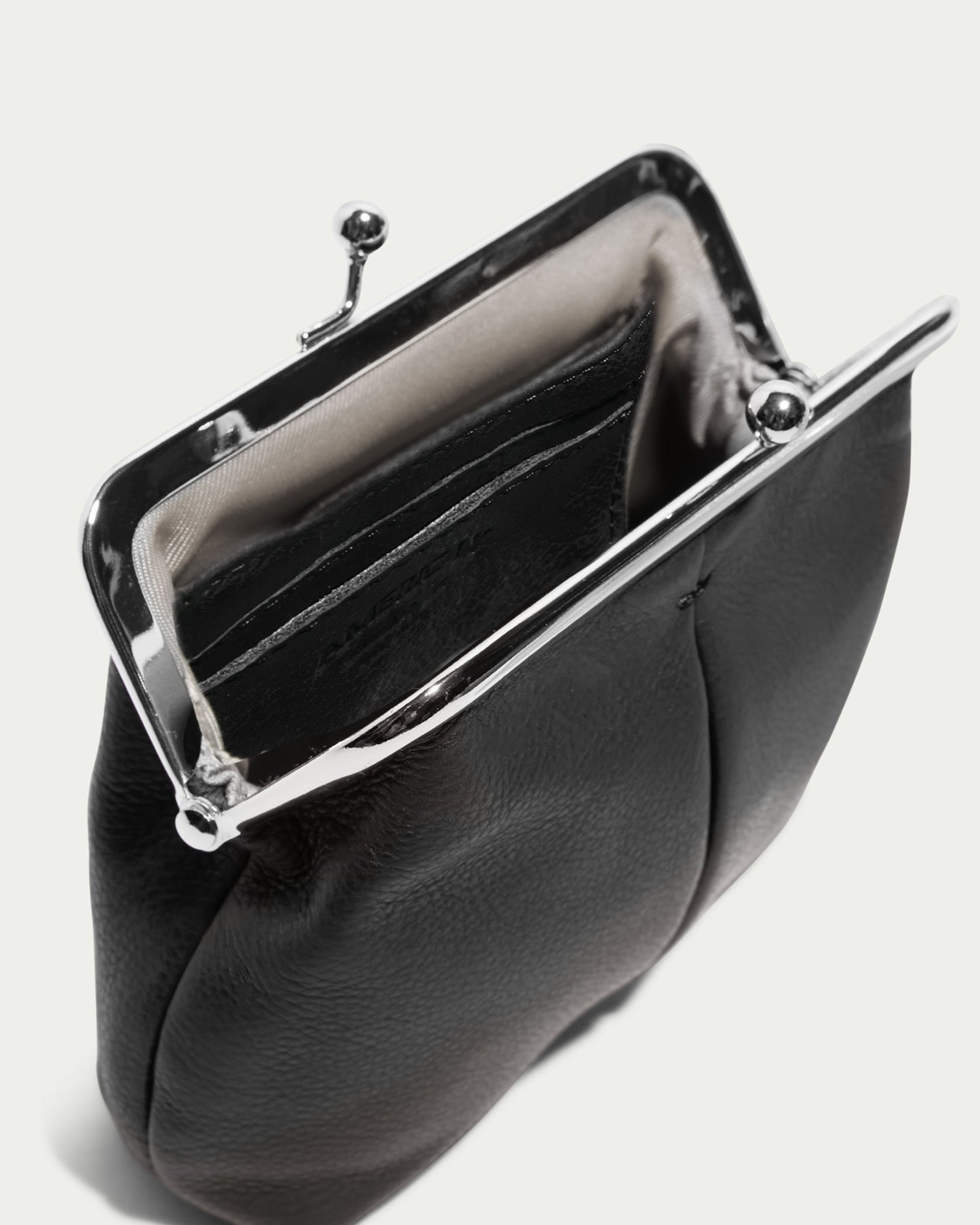 A black leather Wolfe Frame Kisslock With CC Slots from the American Leather Co. is open, revealing a black compartment inside. The purse has a vintage style and a soft, textured exterior. The interior lining is light beige. The purse is set against a plain white background.