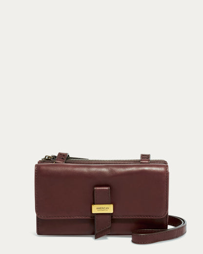 The Essex Wallet Crossbody by American Leather Co. is a compact burgundy leather wristlet crafted from genuine American leather, featuring a zipper and flap closure with a gold-colored label. It includes both a detachable strap and an adjustable crossbody strap against a neutral background.