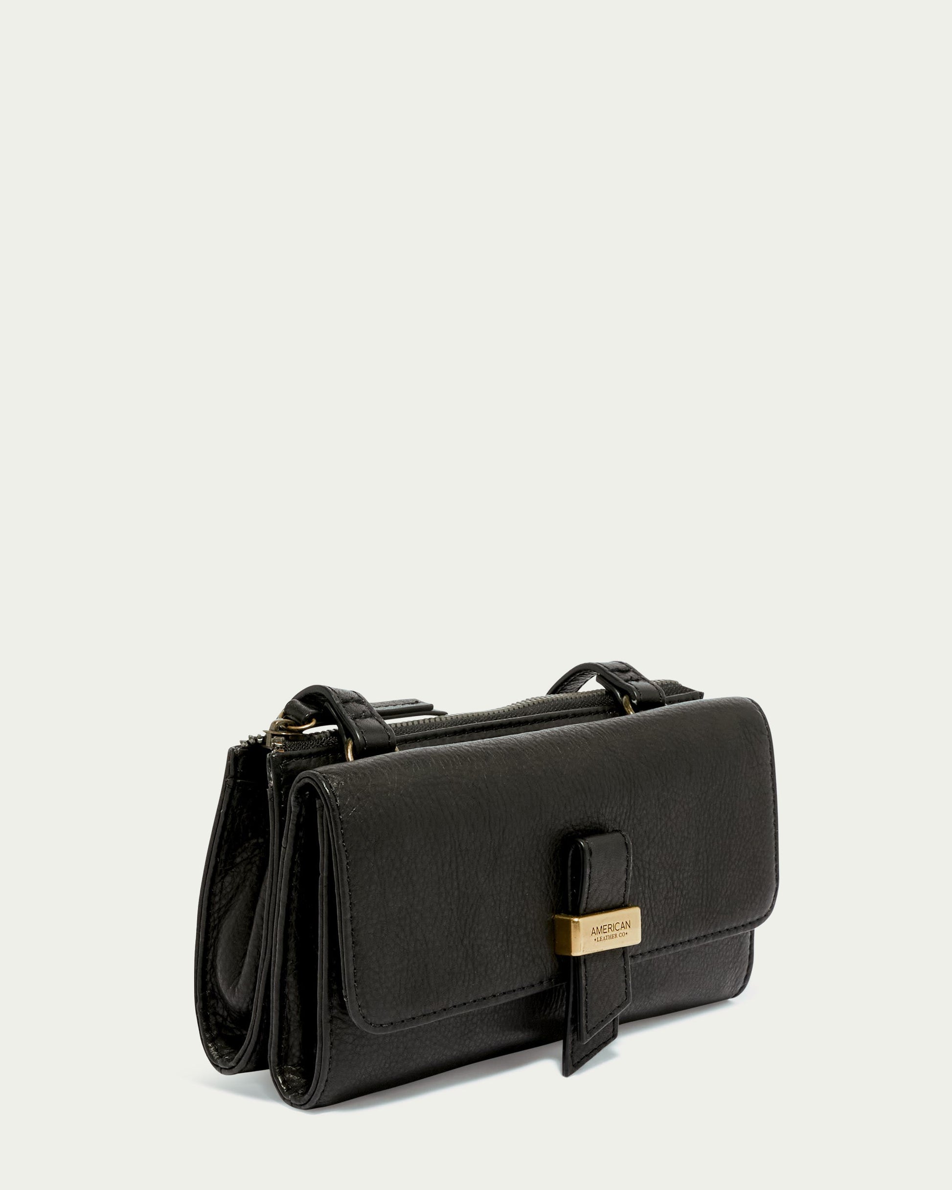 The Essex Wallet Crossbody by American Leather Co. is a stylish black handbag crafted from genuine American leather with a textured surface and gold accent on the front flap. Its sleek design features twin compartments and an adjustable crossbody strap, perfect for casual and formal occasions.