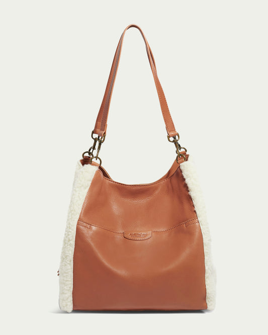 The Austin Triple Entry Hobo by American Leather Co. is a chic casual accessory, featuring genuine brown leather with white fluffy sides, a single shoulder strap, and a front pocket with a decorative brand patch. It has gold-tone hardware and a slouchy design.