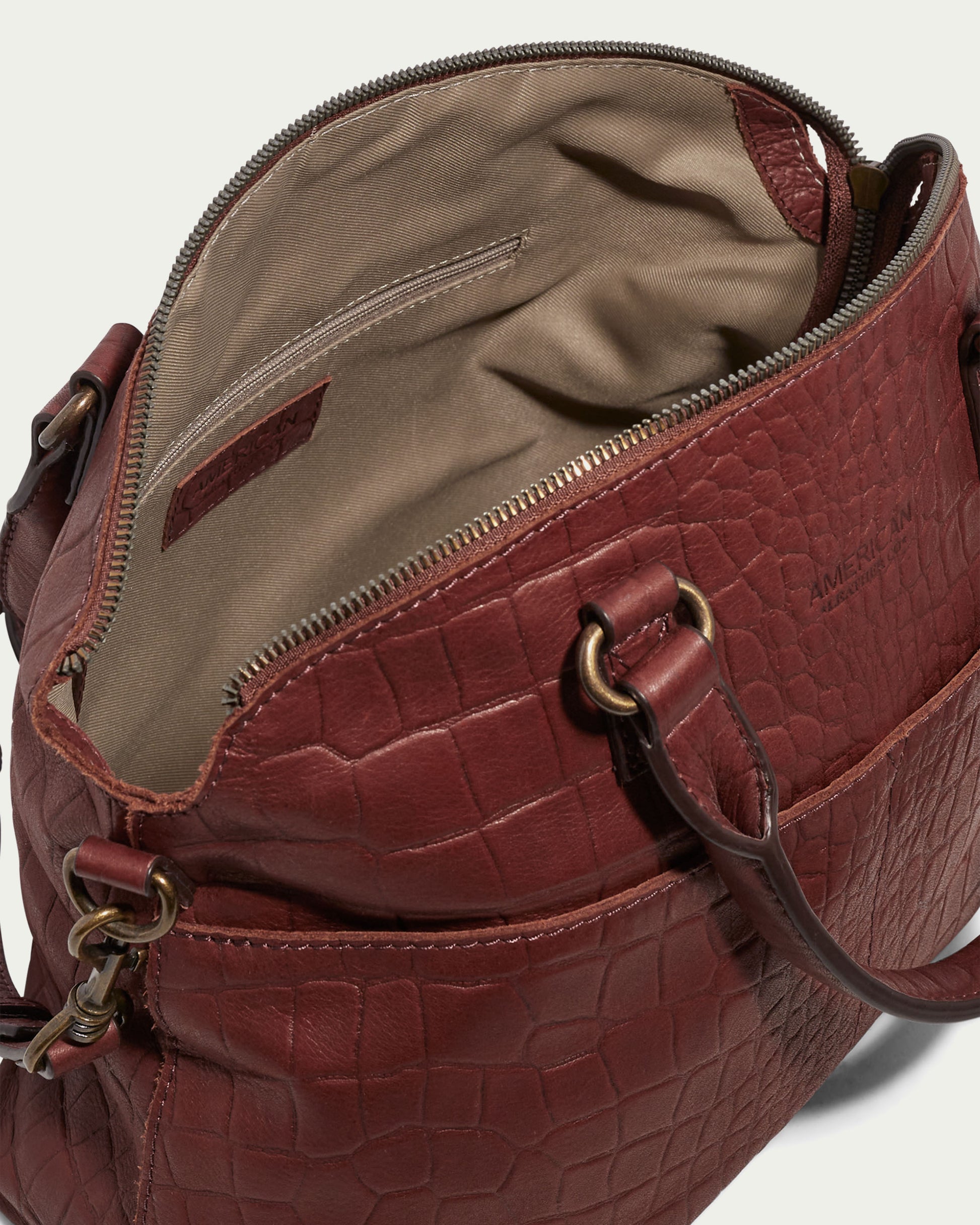 The Carrie Dome Satchel by American Leather Co. is an open brown leather handbag with a crocodile pattern, beige fabric-lined interior, metal rings on the handles, and a small zippered pocket inside.