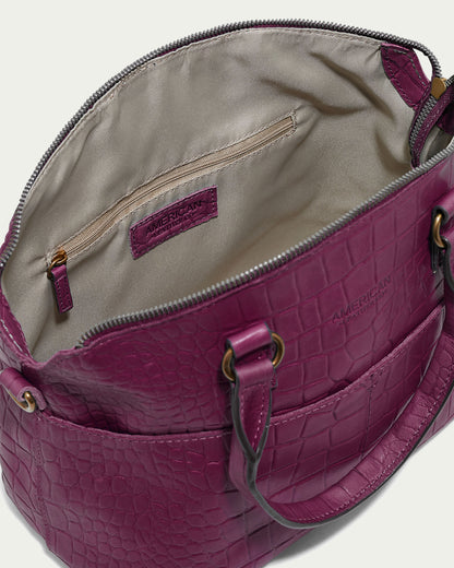 Introducing the Carrie Dome Satchel by American Leather Co., a luxurious handbag crafted from genuine American leather. This elegant purple bag showcases a striking crocodile pattern and an open top, unveiling a beige interior complete with a zippered pocket. It features two sturdy handles and exquisite visible stitching for a sophisticated finish.