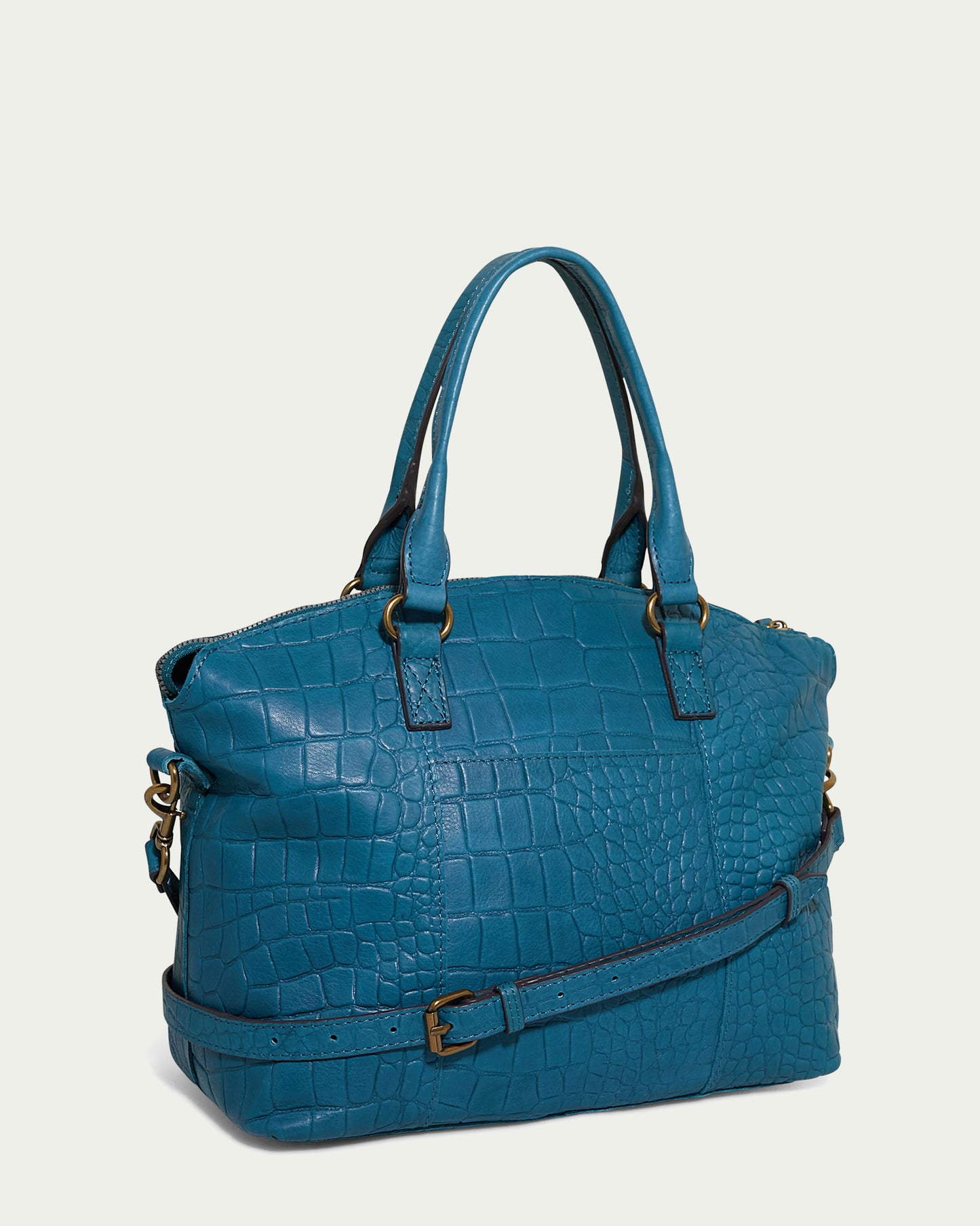 The Carrie Dome Satchel by American Leather Co. is a blue handbag showcasing a textured, crocodile-skin pattern. It features two handles, an adjustable crossbody strap with a brass buckle, and brass hardware accents. Crafted from Genuine American Leather, the bag also includes a zippered top opening.