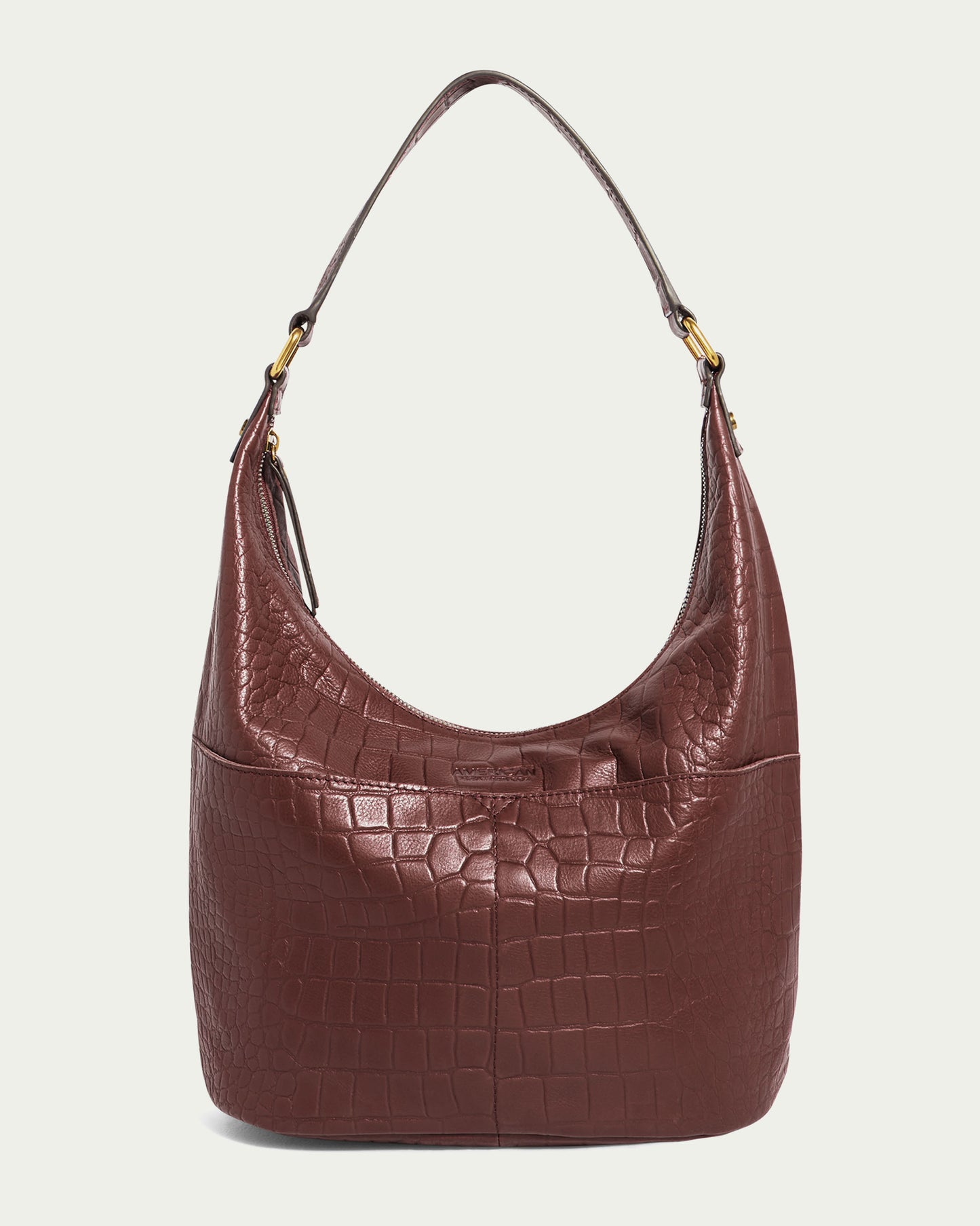 The Carrie Hobo by American Leather Co. showcases a brown crocodile-patterned design with a curved top, complemented by two gold-tone metal rings attaching the shoulder strap. This bag features a smooth, shiny texture and has a zip closure, offering both style and security.