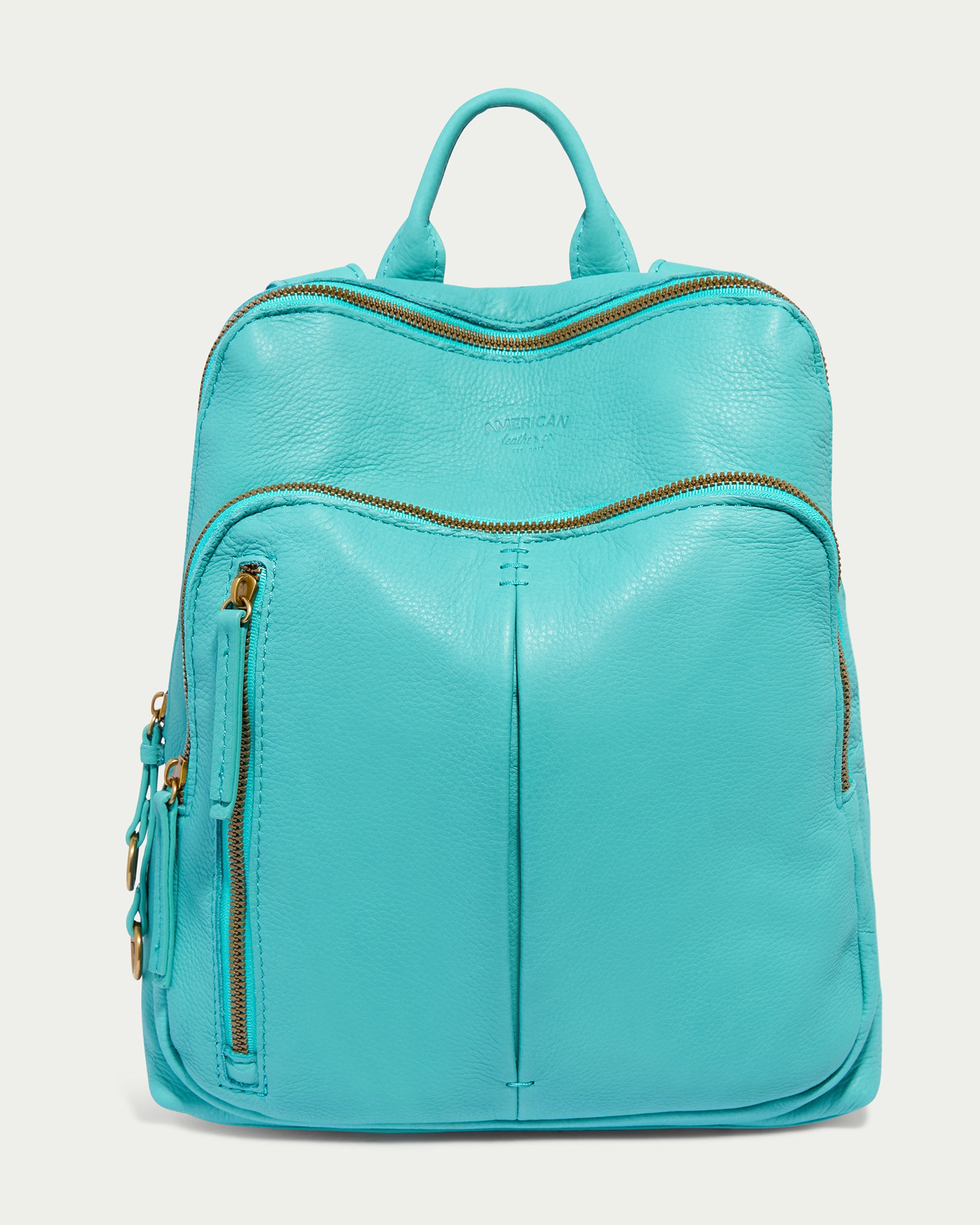 The Cleveland Backpack by American Leather Co. is crafted in a Blue Lagoon leather with a smooth texture and gold zippers. It features a large main compartment, a zippered front pocket, two side pockets, a sturdy top handle, and adjustable back straps for added convenience.