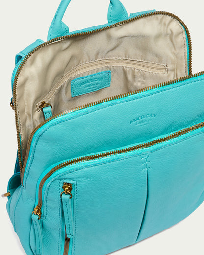 The image features the Cleveland Backpack by American Leather Co., an open turquoise leather backpack purse with multiple compartments. It has gold zippers and stitching on the exterior, a beige fabric lining inside, and a visible label. Its adjustable back straps offer comfort for any adventure.