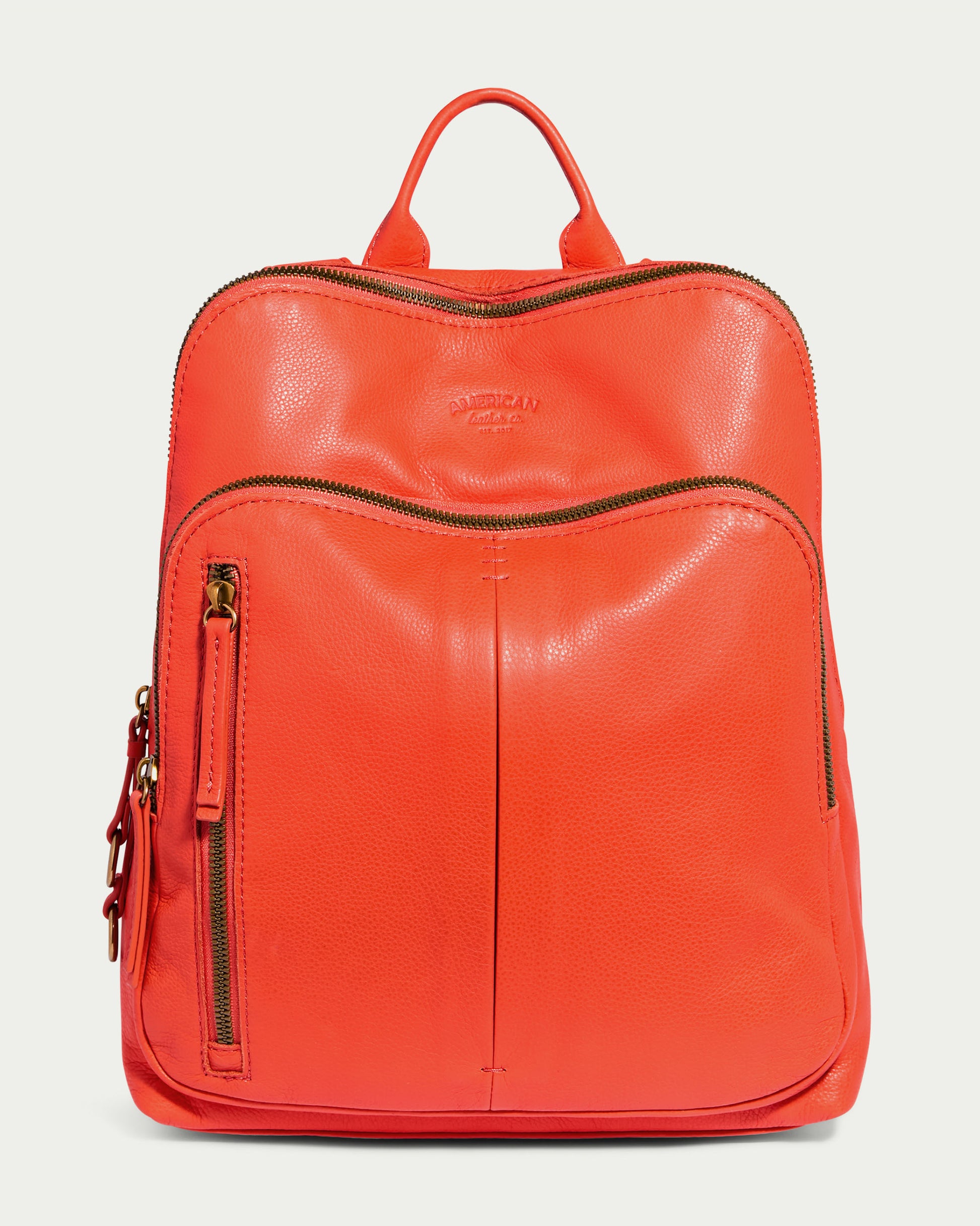 Introducing the Cleveland Backpack by American Leather Co.: a stylish chili red leather backpack purse featuring two zippered compartments, a small front pocket with a zipper, and a top handle. The brand name is embossed on the front, highlighting its genuine leather craftsmanship.