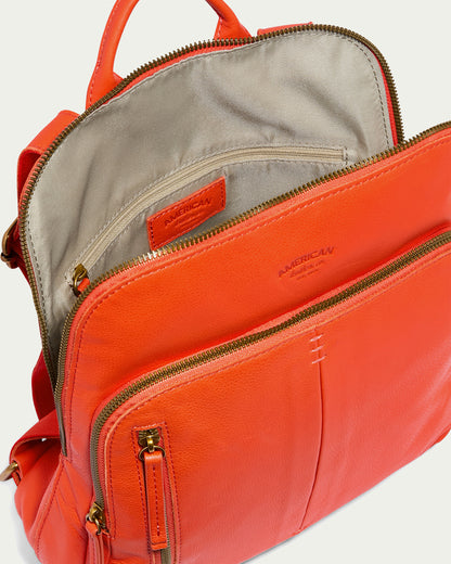 The Cleveland Backpack by American Leather Co. is a stylish accessory crafted from bright orange genuine leather, featuring open compartments that reveal a beige lining and multiple gold zipper pockets. Designed for optimal organization, it also includes a handle at the top and a spacious interior.