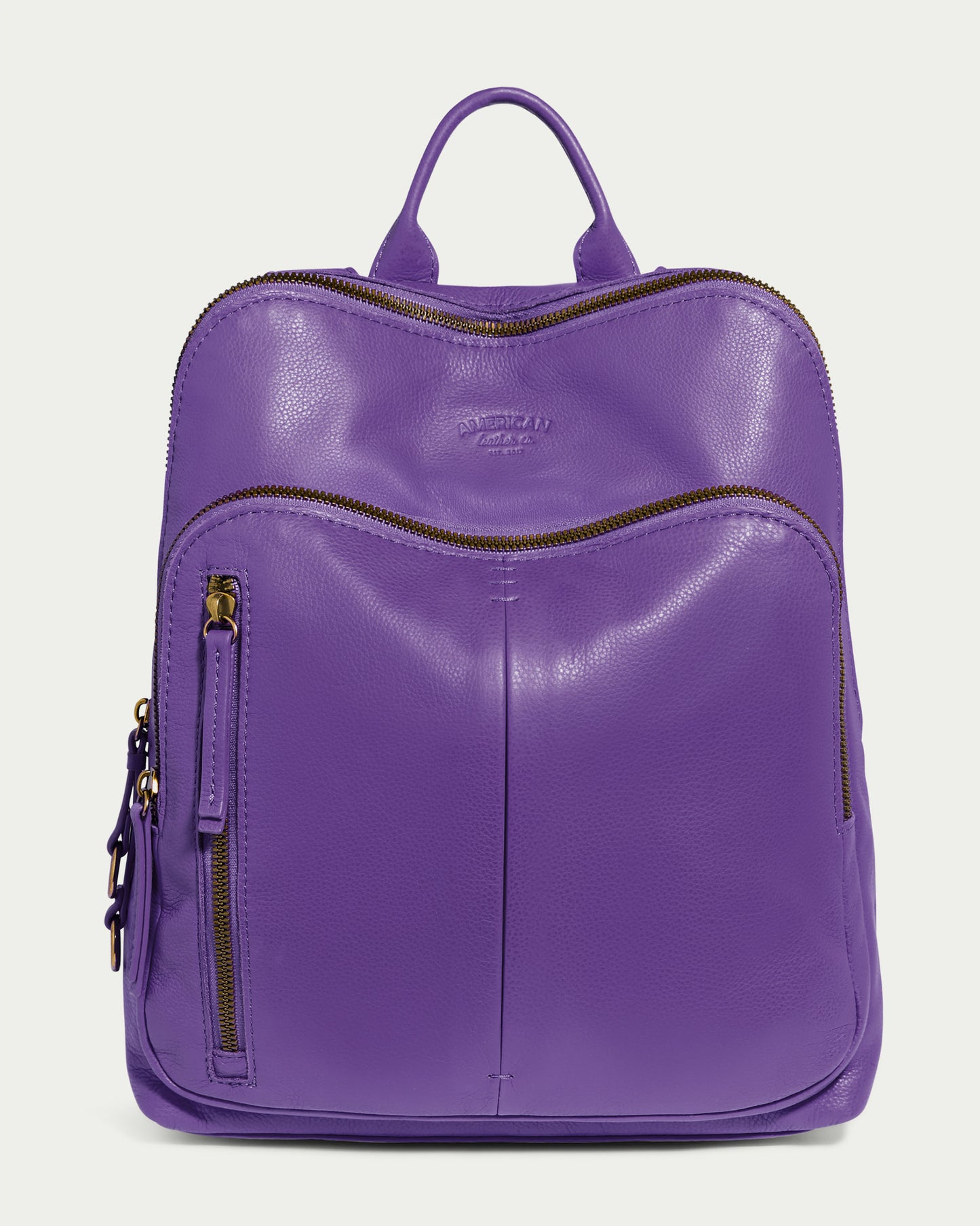 Introducing the Cleveland Backpack by American Leather Co., a grape-colored leather backpack purse with a sleek texture. It features multiple zippered compartments, a convenient small top handle, gold-colored zippers, adjustable back straps, and a minimalist design—all expertly made from genuine leather.