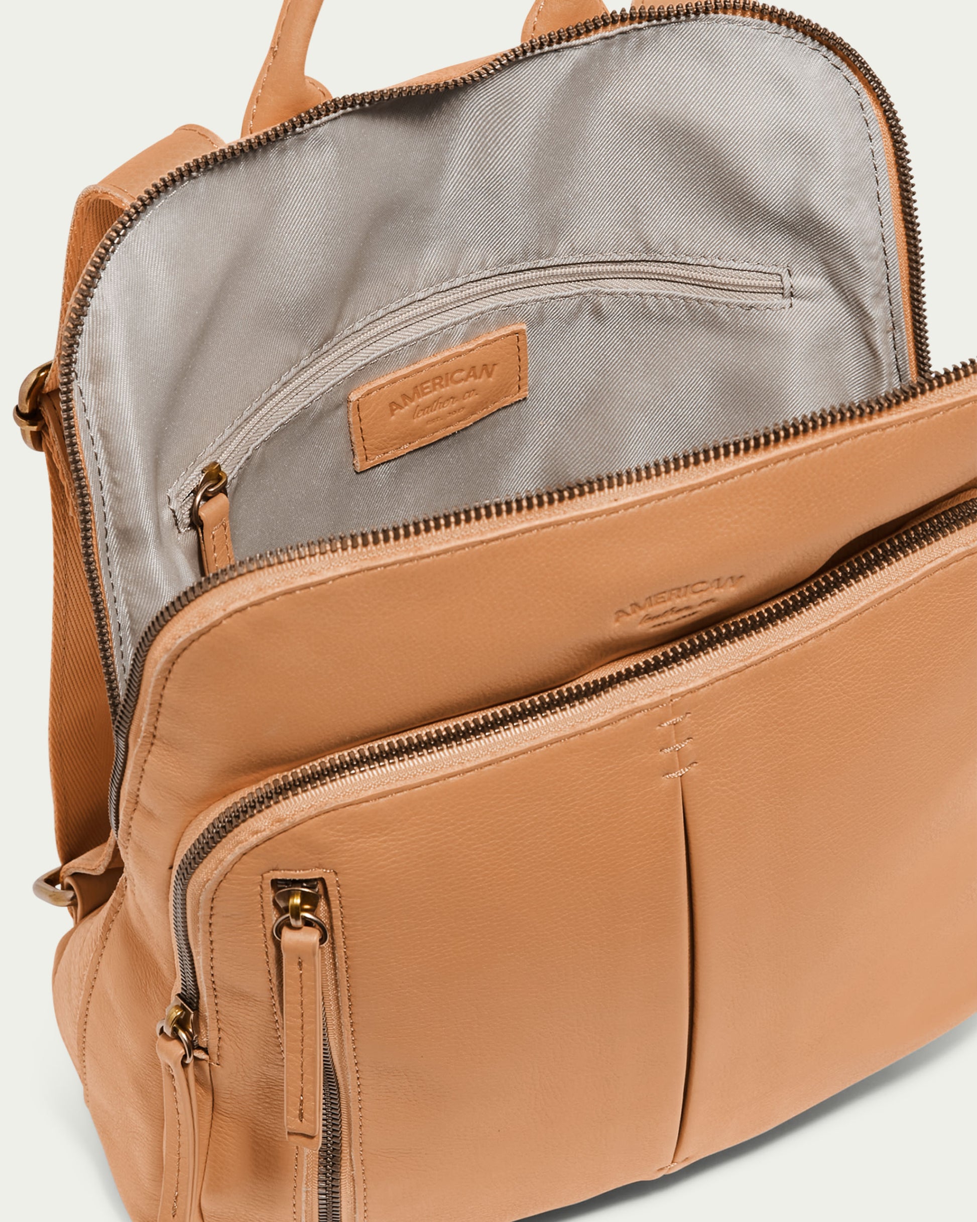 The Cleveland Backpack is made of genuine leather with multiple zip compartments and proudly displays a visible "American Leather Co." label. Its interior boasts a gray lining and includes a zippered pocket, while the exterior highlights a stylish front pocket with two vertical seams, making it both fashionable and functional as a backpack purse.