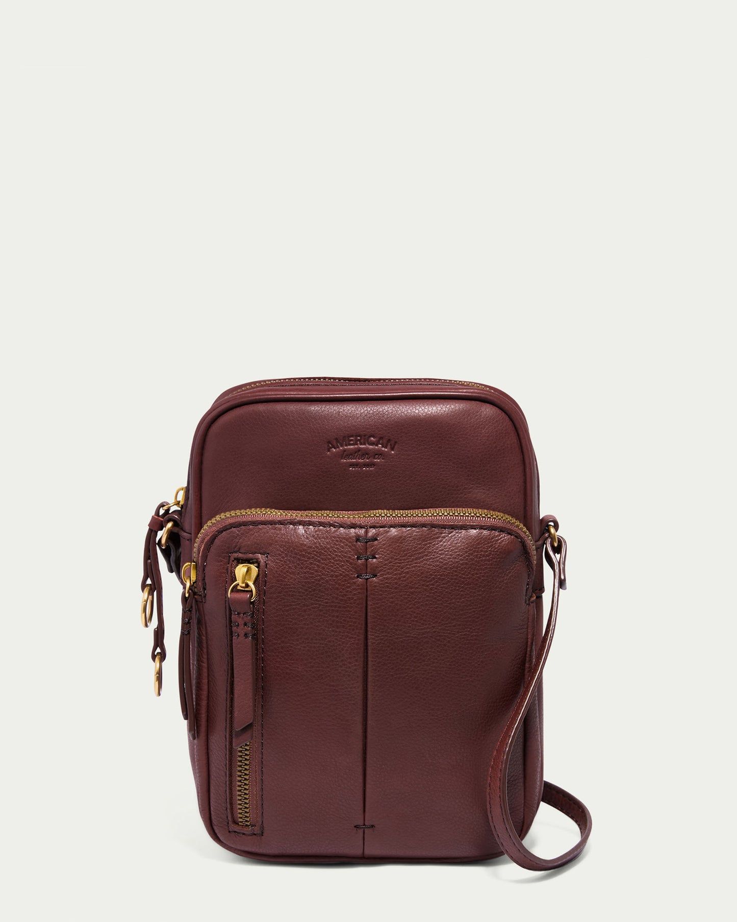 The Cleveland Large NS Crossbody by American Leather Co. is crafted from rich glove leather, featuring a front zip pocket and the embossed phrase "Genuine American Leather Co." It includes a long strap and gold-tone hardware, elegantly displayed on a plain white background.