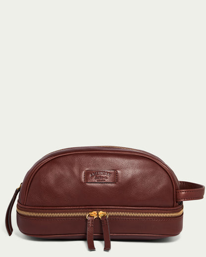 The Shorewood Dopp Kit by American Leather Co. is a brown men's travel companion, made from textured glove leather. It features a side handle, dual zipper compartments with leather pulls, and a stitched label on the front.