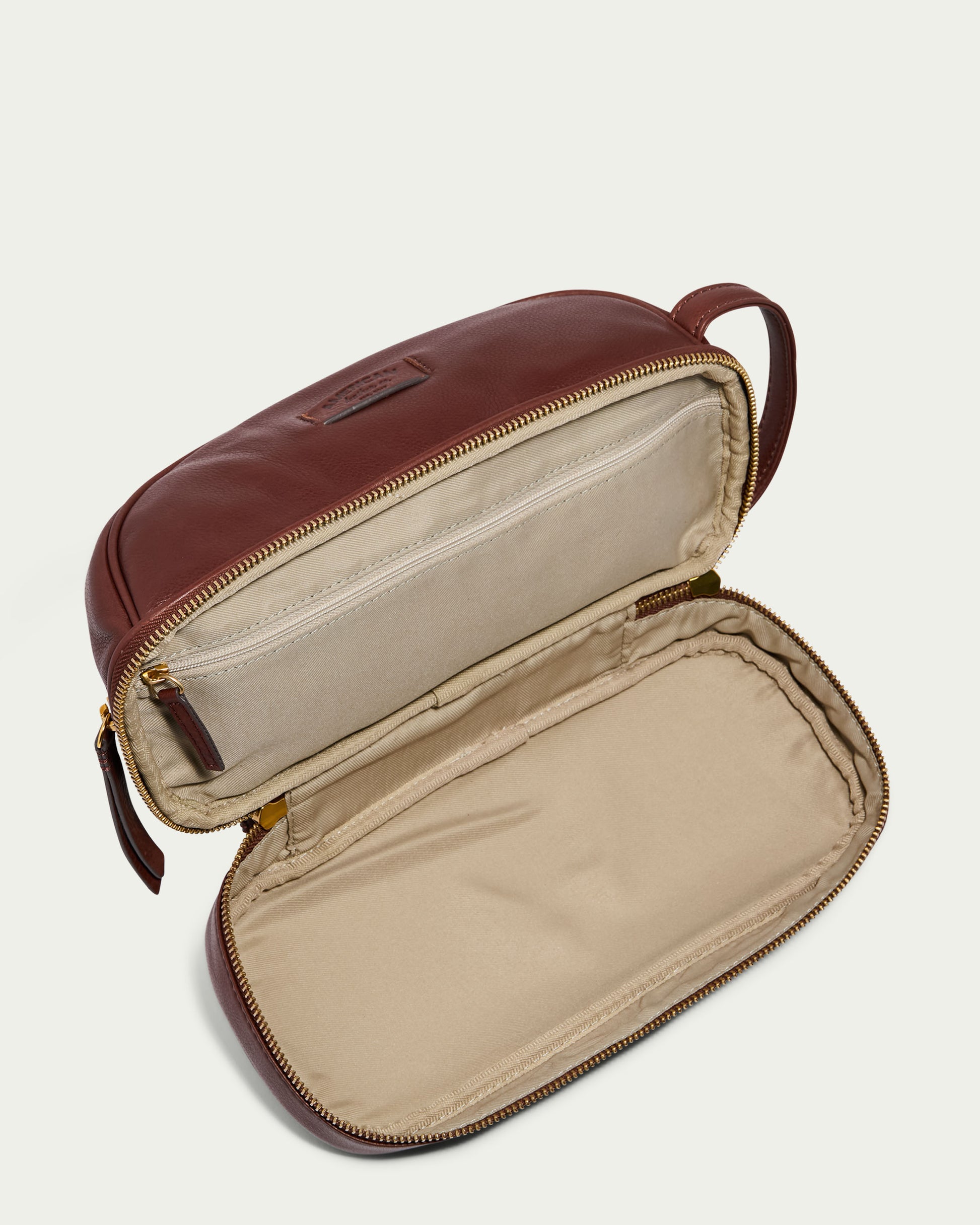 The Shorewood Dopp Kit by American Leather Co. opens to showcase its beige interior. This brown leather toiletry bag, perfect for men, includes a zipper and handle on one end, making it an ideal travel companion that's ready for packing.