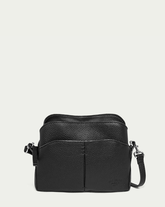 The Tulip Triple Entry Crossbody by American Leather Co. is a black genuine leather bag with a textured finish, featuring a main compartment, front pocket, and an adjustable strap with silver-tone hardware, set against a plain white background.