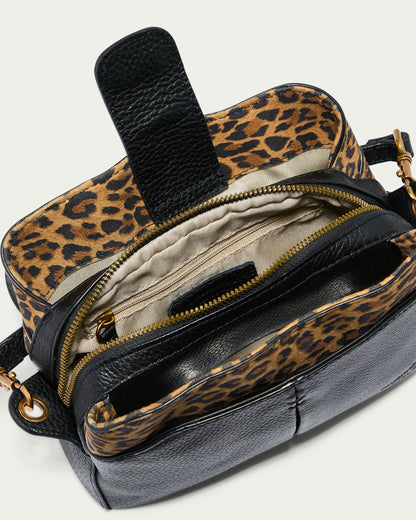 Introducing the Tulip Triple Entry Crossbody by American Leather Co., a sleek black bag made from genuine leather. It boasts a gold zipper and a stylish leopard print interior lining. The open design reveals several compartments and includes an adjustable strap for versatile wear.