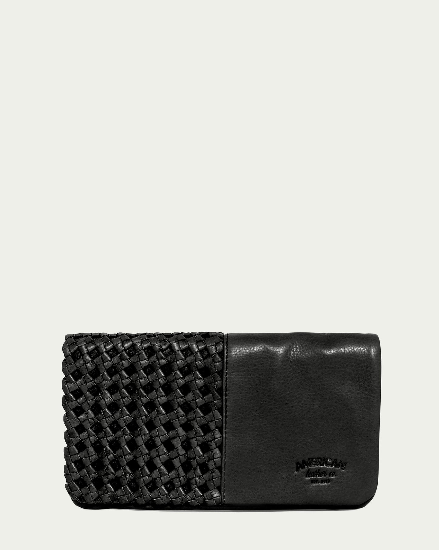 Introducing the Webster Woven Bifold Wallet by American Leather Co., a stylish black leather accessory featuring a textured woven pattern on one side and smooth leather on the other. Inside, it offers convenient credit card slots for organization. The brand name is subtly embossed in small letters on the lower right corner. It is displayed against a plain off-white background.