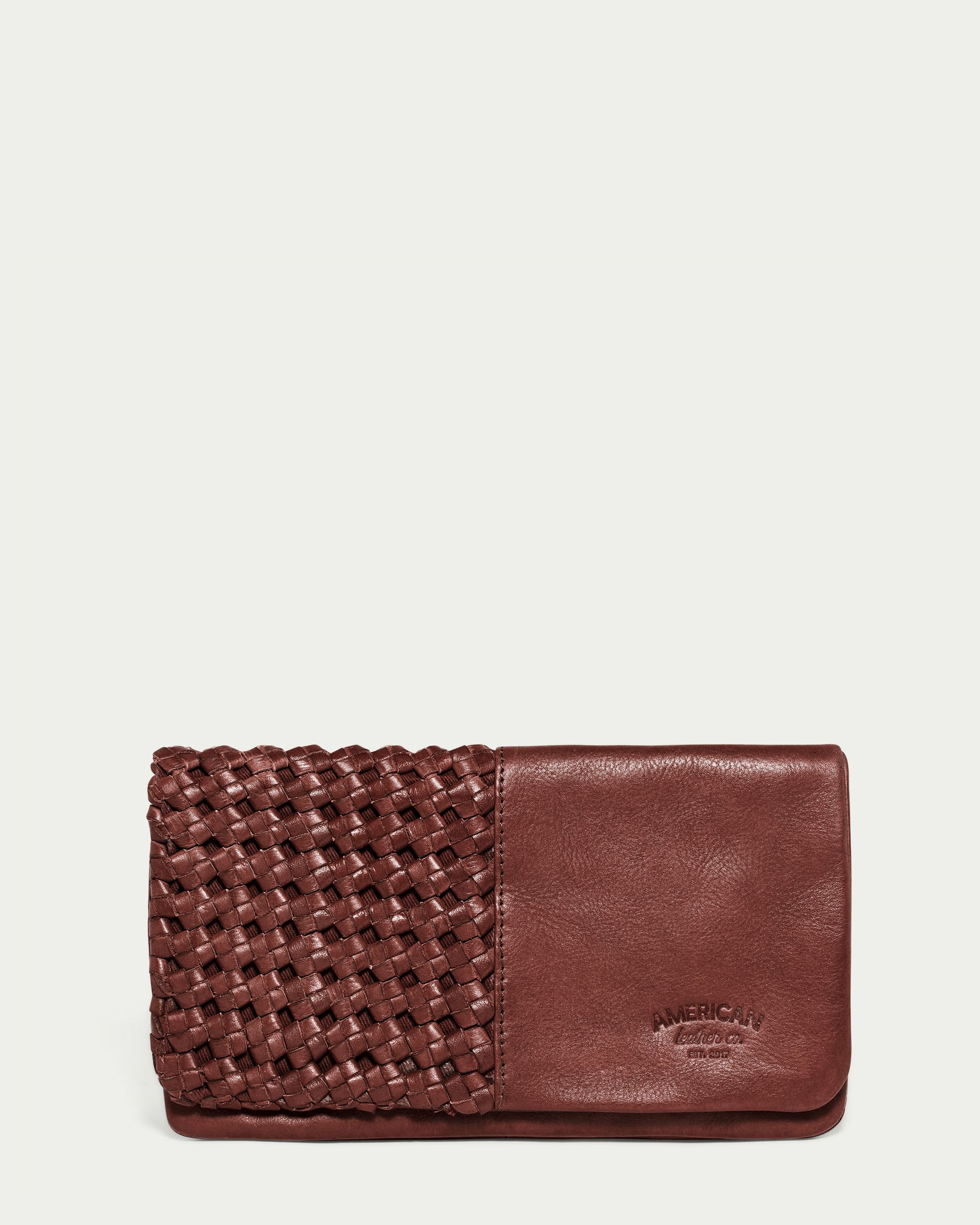 The Webster Woven Bifold Wallet by American Leather Co. showcases supple leather with a distinctive woven design on the left side and a smooth finish on the opposite side. The brand name, "American Leather Co.," is subtly embossed in the lower right corner, adding an elegant touch to this Cordovan-colored wallet.