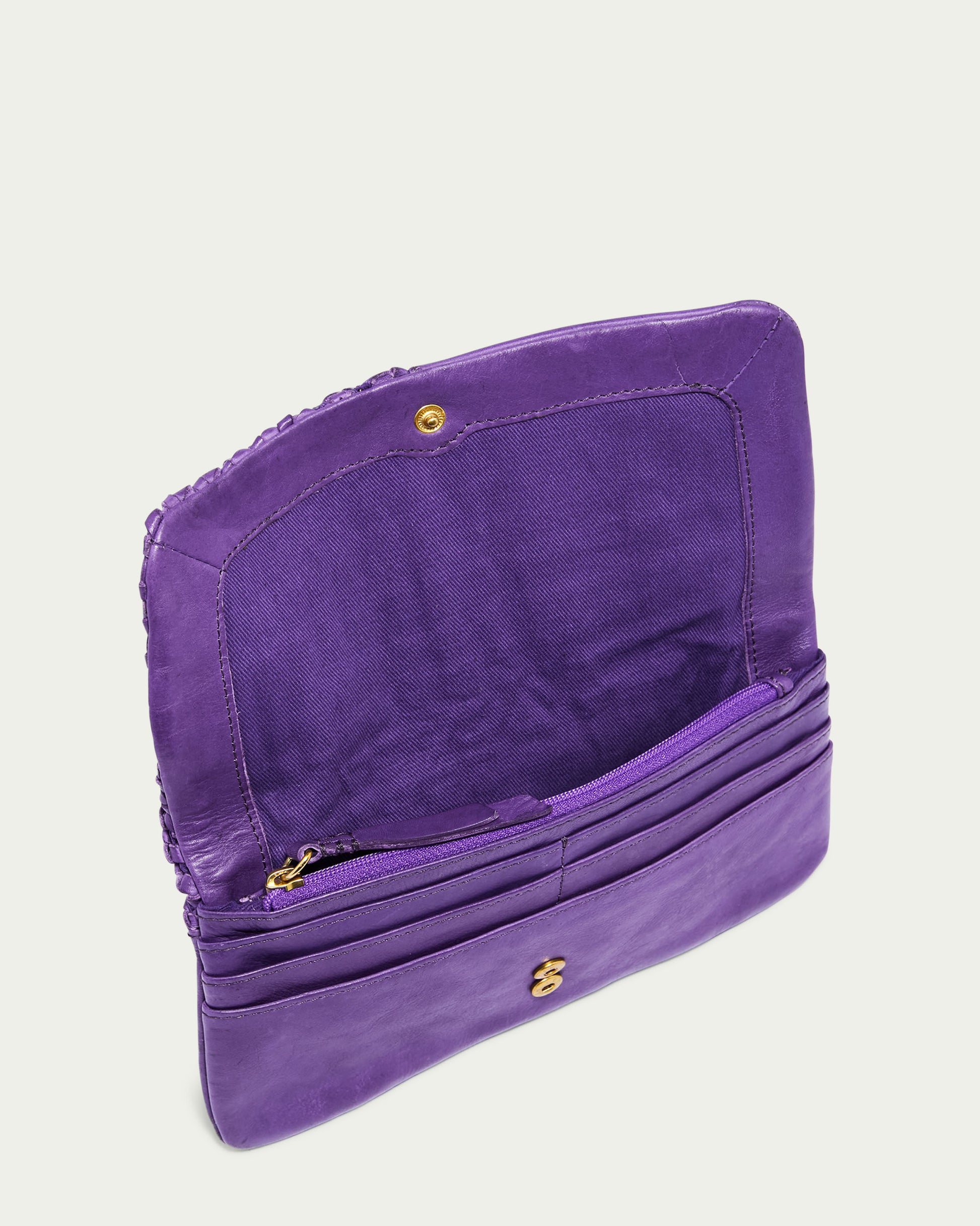 The Webster Woven Bifold Wallet by American Leather Co. is open, revealing its purple leather design with multiple credit card slots, a zippered compartment, and a fabric-lined interior featuring woven details. The main flap is open, highlighting its organized sections with a secure snap closure.