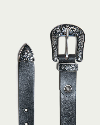 The close-up of the Hamilton Belt by American Leather Co., a true wardrobe essential, highlights its polished silver hardware. The buckle features intricate floral engravings and several holes for adjustable sizing, with the tip mirroring the same floral design.