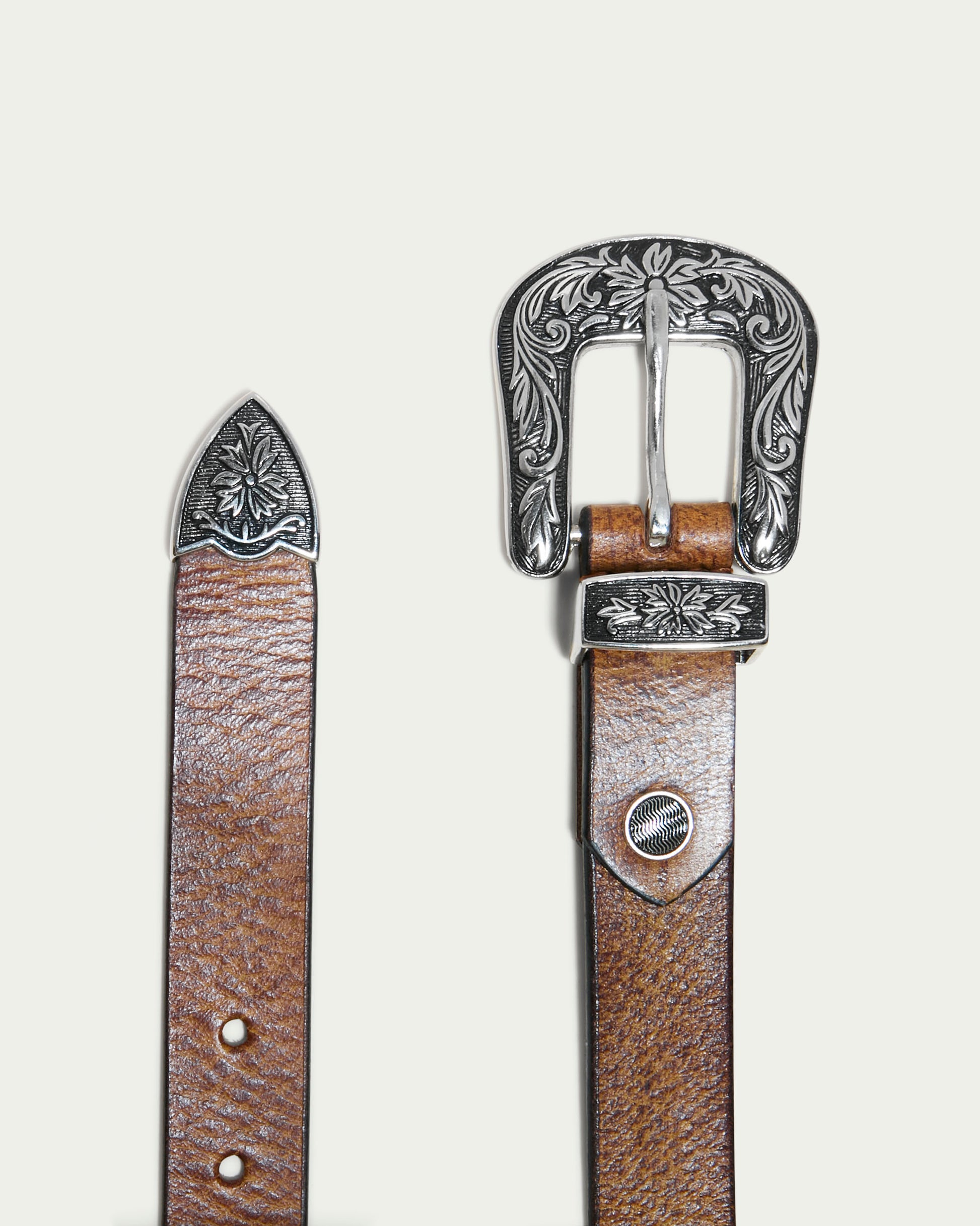 The Hamilton Belt by American Leather Co. is a brown leather accessory with polished hardware, featuring ornate silver buckle and tip with intricate floral designs; a wardrobe essential showcased on a light background, merging classic style and elegance.