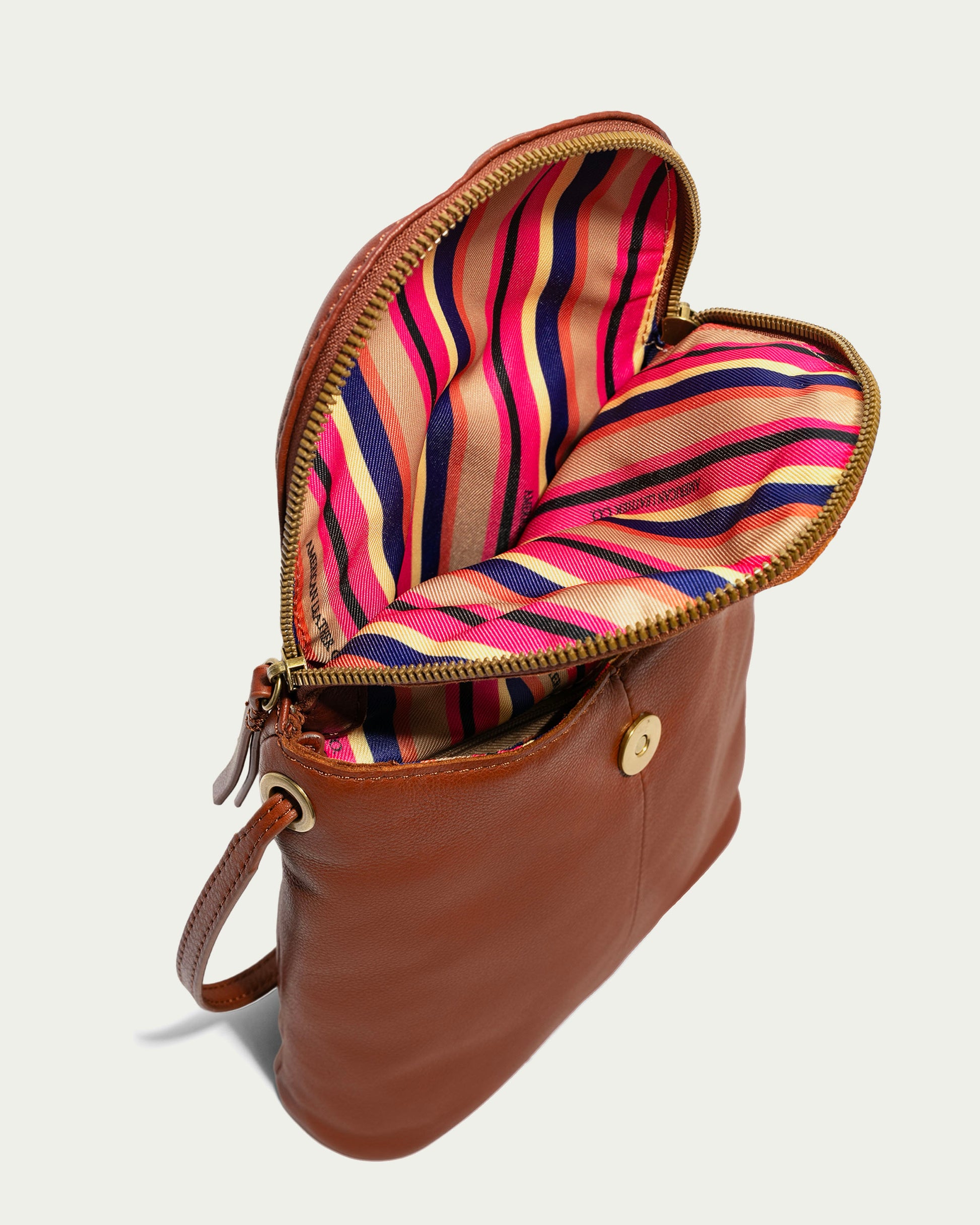 The Hampton Large Zip-Around Crossbody by American Leather Co. is a brown leather crossbody bag made from genuine glove leather, featuring both a flap and zipper closure. Inside, you'll find a vibrant interior adorned with pink, orange, blue, and beige stripes. The bag includes a button detail for added style and has an adjustable crossbody strap for versatile wear.