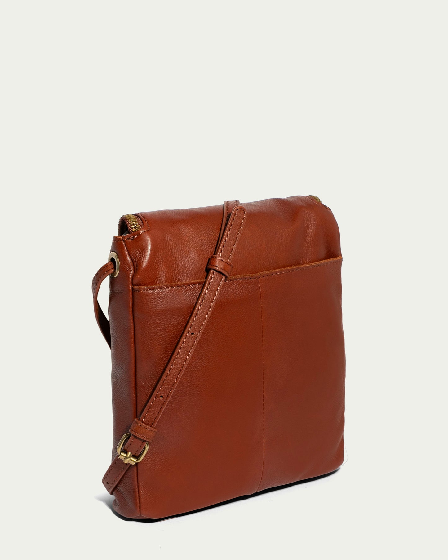 The Hampton Large Zip-Around Crossbody by American Leather Co. is a chic brown crossbody bag made from genuine glove leather, featuring a gold buckle on its adjustable strap. It showcases a sleek design with a visible seam down the center and a top zipper, set against a light neutral background.