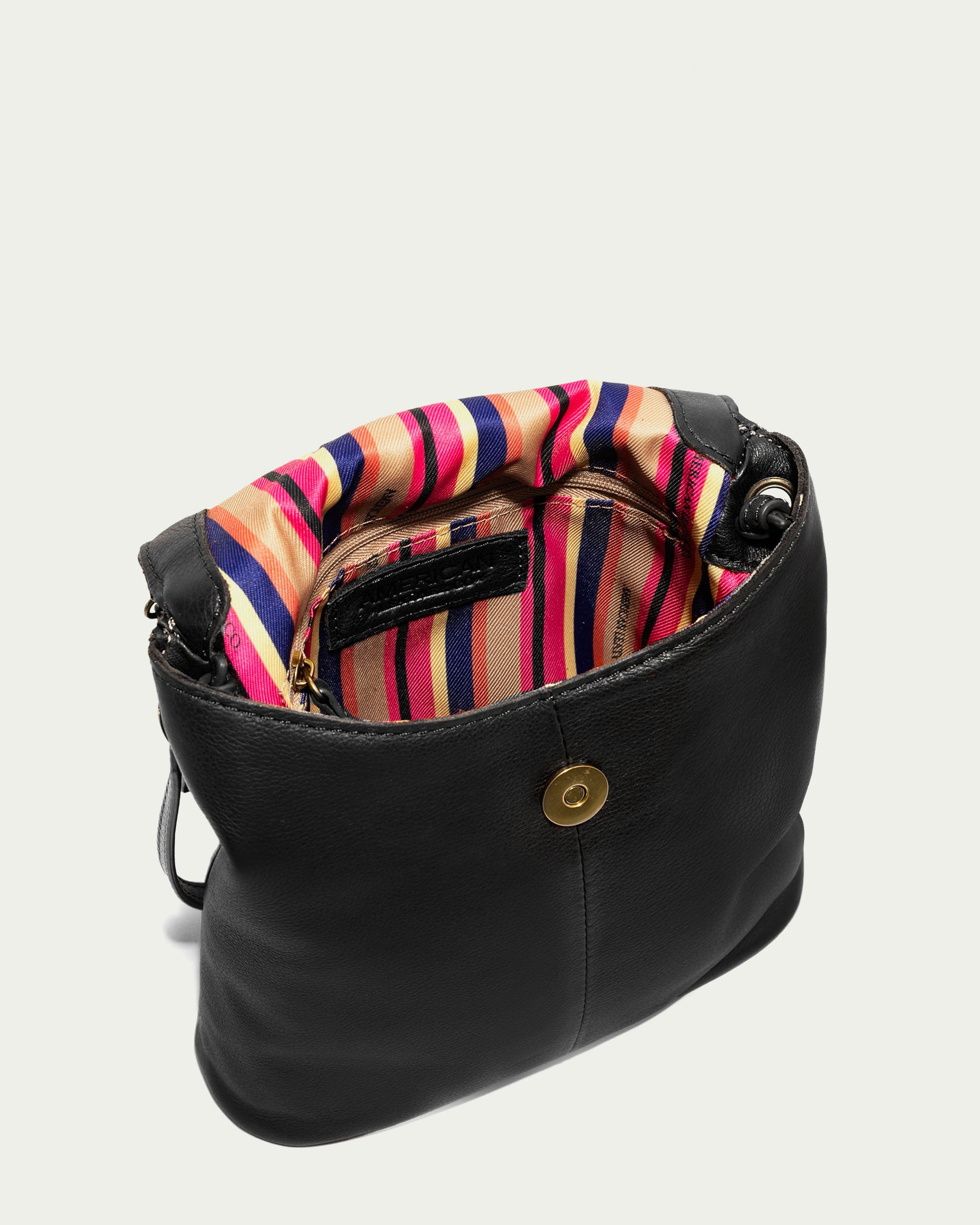 The Hampton Large Zip-Around Crossbody by American Leather Co. is open, showcasing a vibrant interior with vertical stripes in red, blue, orange, and pink. Inside, there’s a small zippered pocket for convenience, and the exterior features a round metal clasp on the front. An adjustable strap provides comfortable crossbody wear.