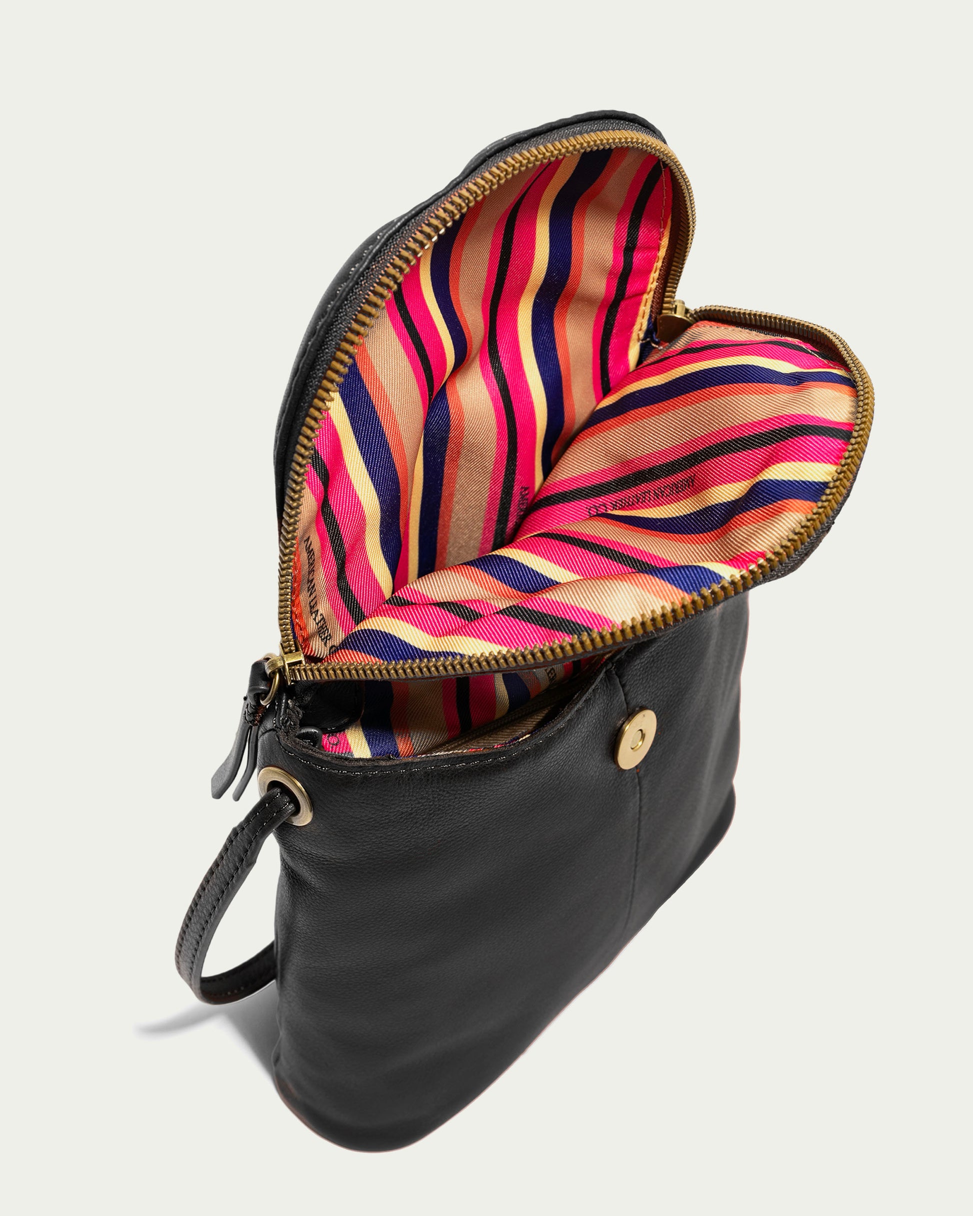 The Hampton Large Zip-Around Crossbody by American Leather Co. is a stylish black leather handbag with a slightly open zipper, showcasing a vibrant interior of red, pink, and beige stripes. It includes a convenient small front pocket with button closure and an adjustable strap for versatile styling.