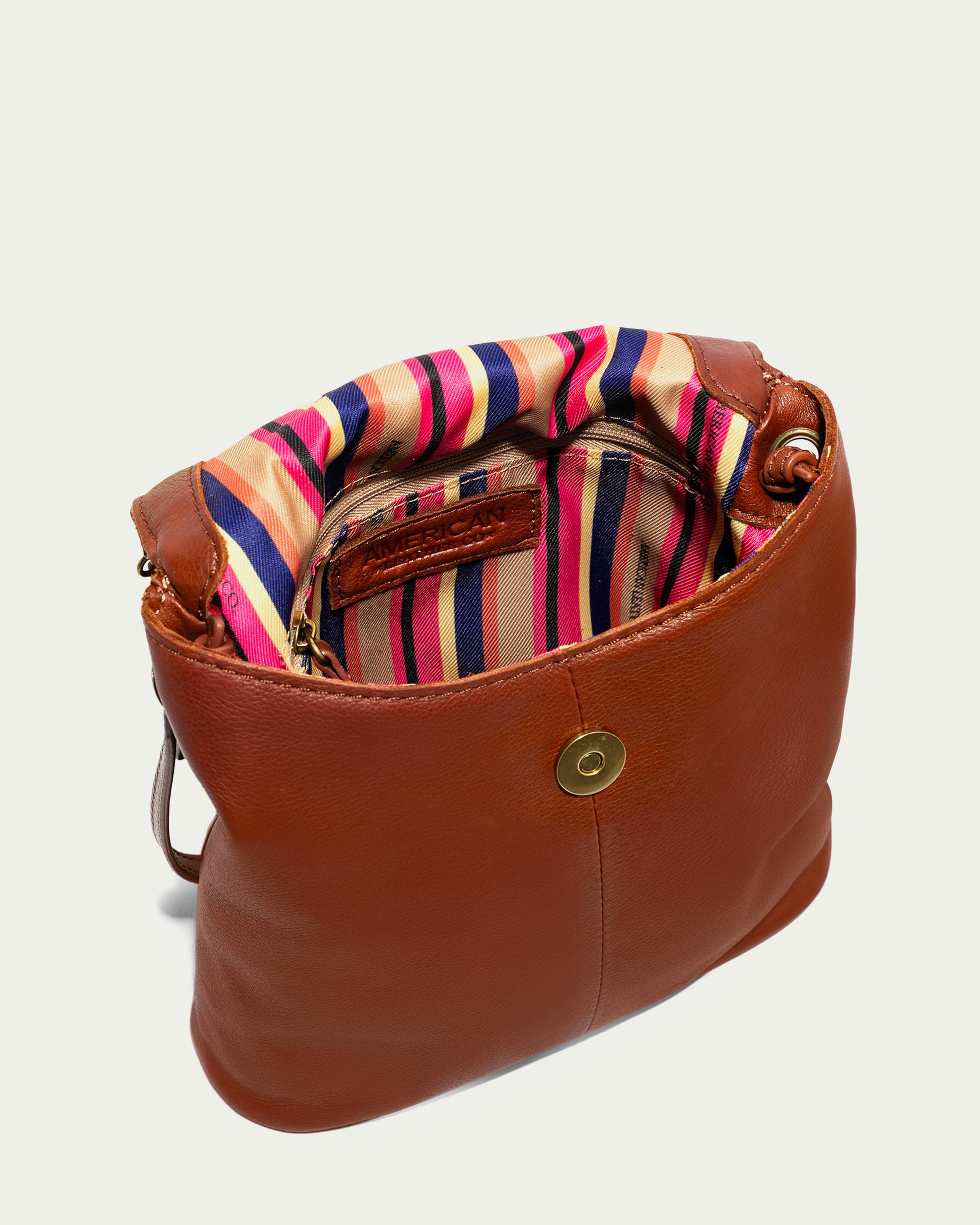 The Hampton Large Zip-Around Crossbody by American Leather Co. is expertly crafted from genuine glove leather and includes an open top that reveals a vibrant striped interior in pink, red, and blue. Featuring a magnetic clasp and a small pocket inside, this stylish accessory balances elegance with practicality.