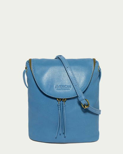 The Hampton Large Zip-Around Crossbody from American Leather Co. is a blue leather handbag made from genuine glove leather, featuring a flap-top design with gold buckle and zipper details. It includes an adjustable crossbody strap with tassel accents, and the brand name "American Leather Co." elegantly embossed on the flap.