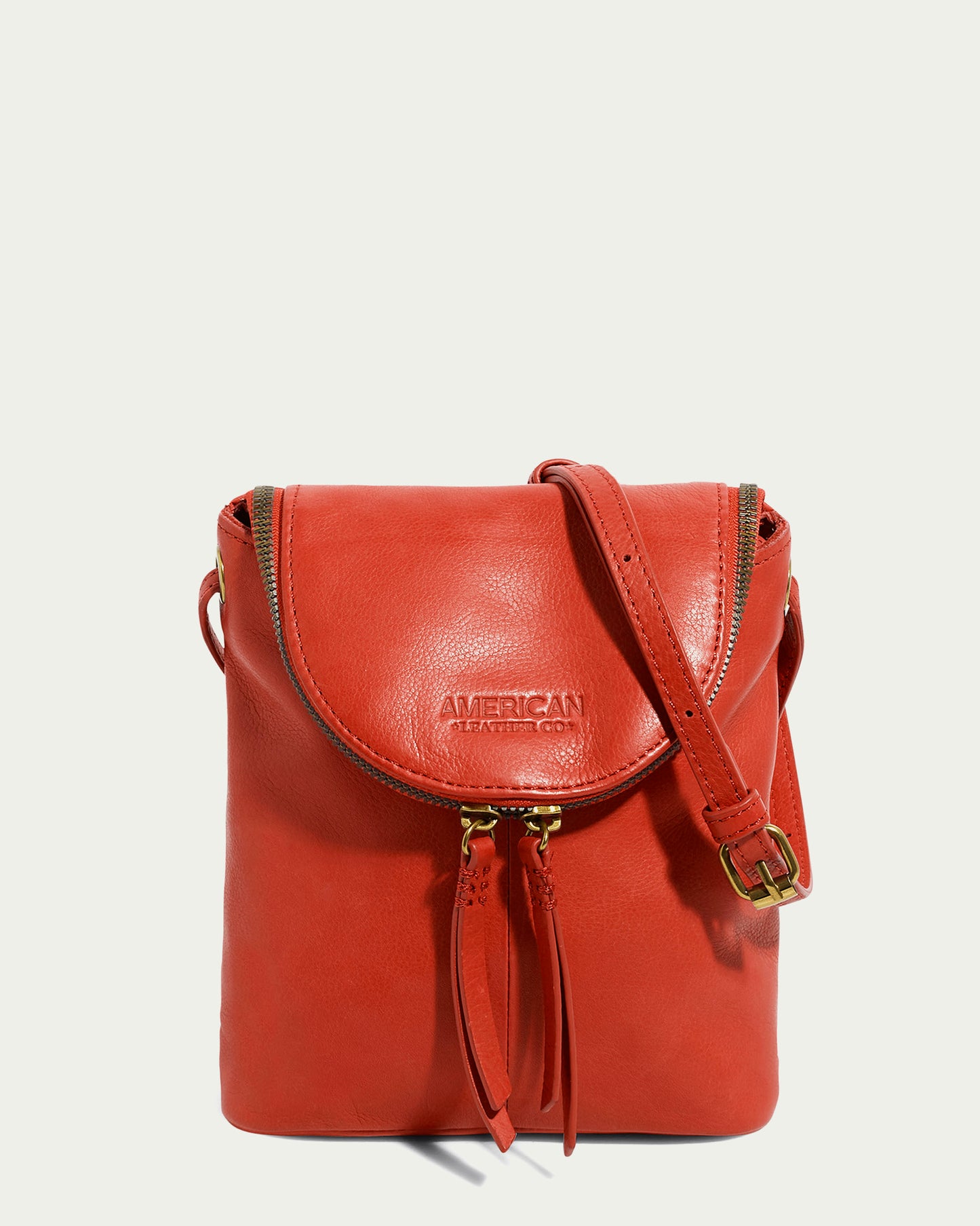 The American Leather Co. Hampton Large Zip-Around Crossbody in genuine glove leather showcases a flap closure and an adjustable strap. Its front design includes embossed text and dual zippers with tassel-style pulls, seamlessly blending simplicity and elegance.