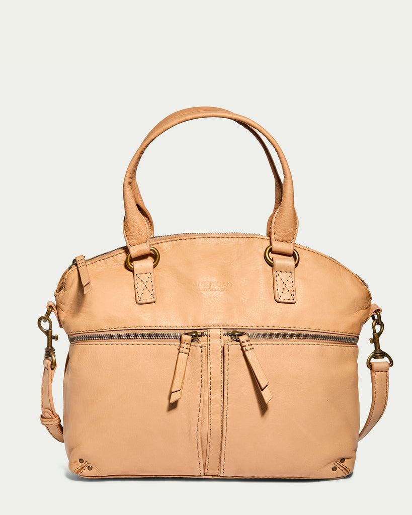 The Hanover Dome Satchel by American Leather Co. is a tan leather handbag with short handles and a detachable, adjustable shoulder strap. This genuine American leather bag features a top zipper closure and a front pocket with dual zipper pulls. Its smooth leather is complemented by minimal stitching details and small metal stud accents at the base.