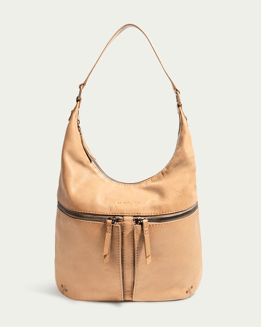 Introducing the Hanover Hobo by American Leather Co., a tan leather shoulder bag featuring a single strap. The front showcases symmetrical zippered pockets with leather pull tabs, enhancing its functional design. Crafted from Genuine American Leather, the bag boasts a slightly slouchy, casual aesthetic with soft creases and a smooth finish. Photographed against an off-white background, this accessory perfectly marries style and practicality.