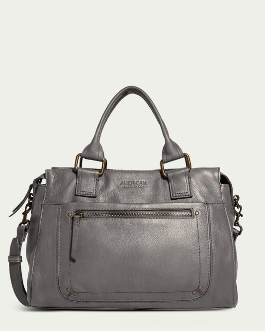 Introducing the Jamestown Satchel by American Leather Co., a stylish top handle satchel crafted in genuine American leather. This chic bag features a sophisticated gray hue and comes with a detachable, adjustable shoulder strap. It also boasts a front zipper pocket with gold-tone hardware and decorative stitching, while the brand name "American Leather Co." is embossed beneath the handles.