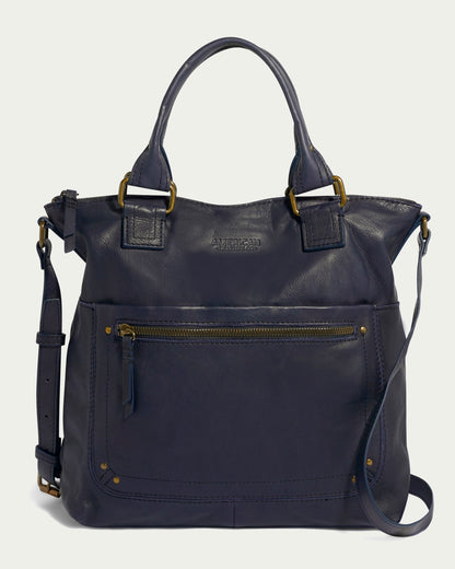 The Jamestown Tote by American Leather Co. is an elegant dark blue handbag made from authentic American leather. It includes durable handles and an adjustable shoulder strap, featuring a top zip closure and a front zip pocket with brass hardware accents, along with a prominently embossed logo above the pocket.