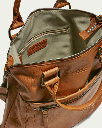 A brown Jamestown Tote with a partially open zipper, revealing an inner pocket with a fabric lining. The handbag features sturdy handles, a front zippered pocket, and a stitched label indicating it is made by American Leather Co.