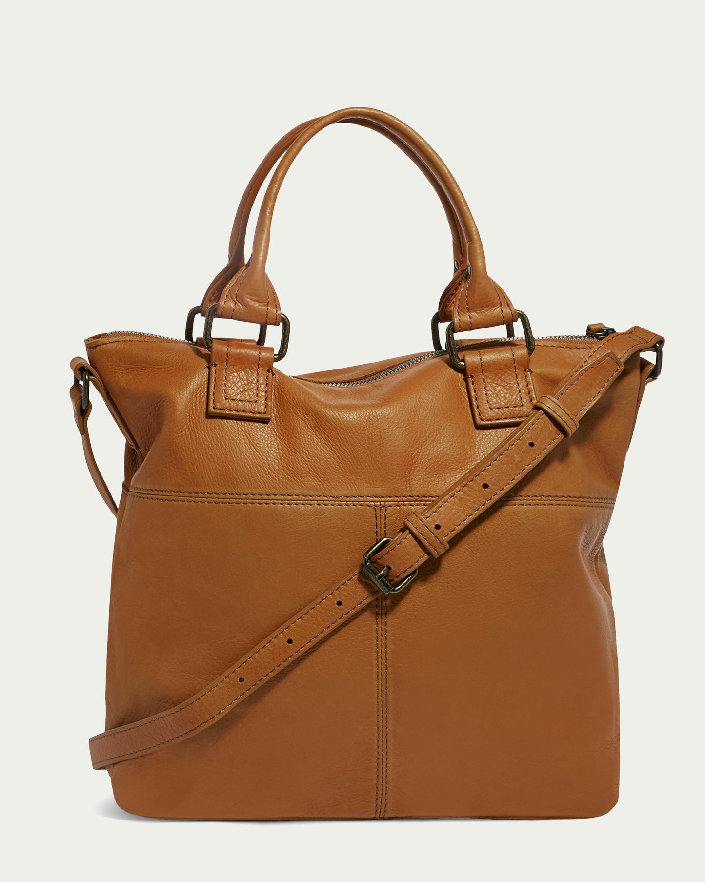 The Jamestown Tote by American Leather Co. is a stylish handbag crafted from tan-colored Genuine American Leather, featuring two short handles and a long, adjustable shoulder strap. The bag showcases a top zip closure and a minimalistic, clean design with subtly visible seams running vertically and horizontally on the front.