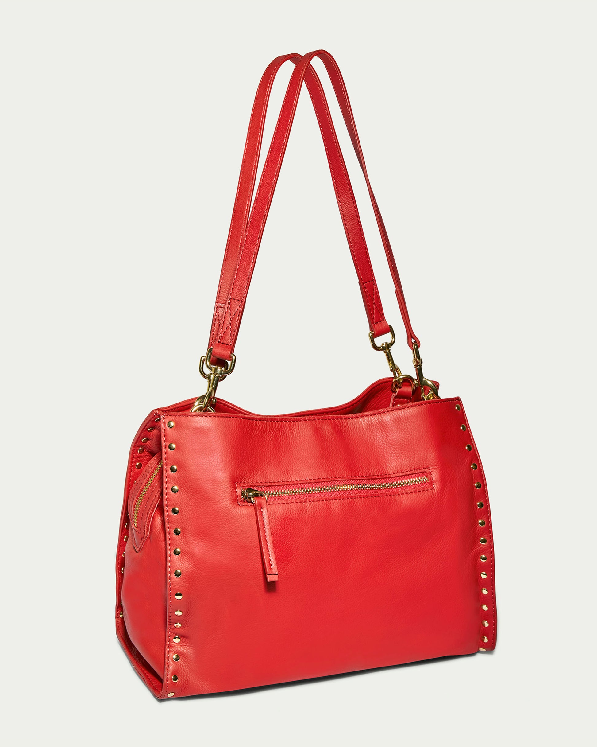 Introducing the Lenox Studded Triple Entry Satchel by American Leather Co., crafted from vibrant genuine red leather with dual straps and gold rivet detailing. This handbag includes an exterior zip pocket on one side and sleek, stylish lines, giving it a modern and elegant appearance.