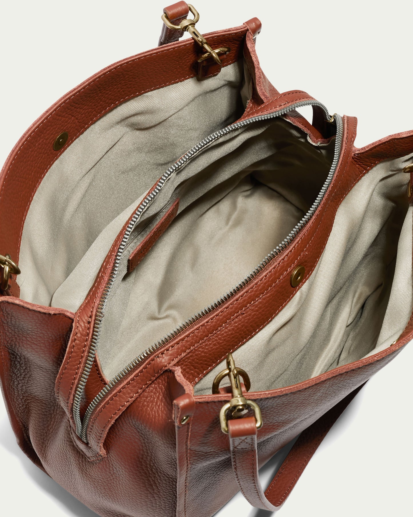 The Lenox Triple Entry Satchel by American Leather Co. is a stylish handbag crafted from genuine American leather, featuring gold hardware and an open design that reveals its spacious beige interior. This elegant satchel boasts multiple compartments, including a central zippered section, and is designed with shoulder straps for comfortable carrying.