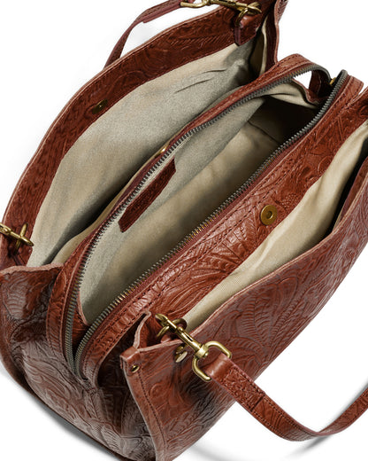 Top view of the Lenox Triple Entry Satchel, an everyday essential by American Leather Co. This brown leather handbag showcases embossed patterns and is crafted from genuine American leather. It includes a zipped main compartment, two smaller interior pockets, gold-tone hardware, and a beige fabric lining. The partially visible shoulder strap adds to its sophisticated design.